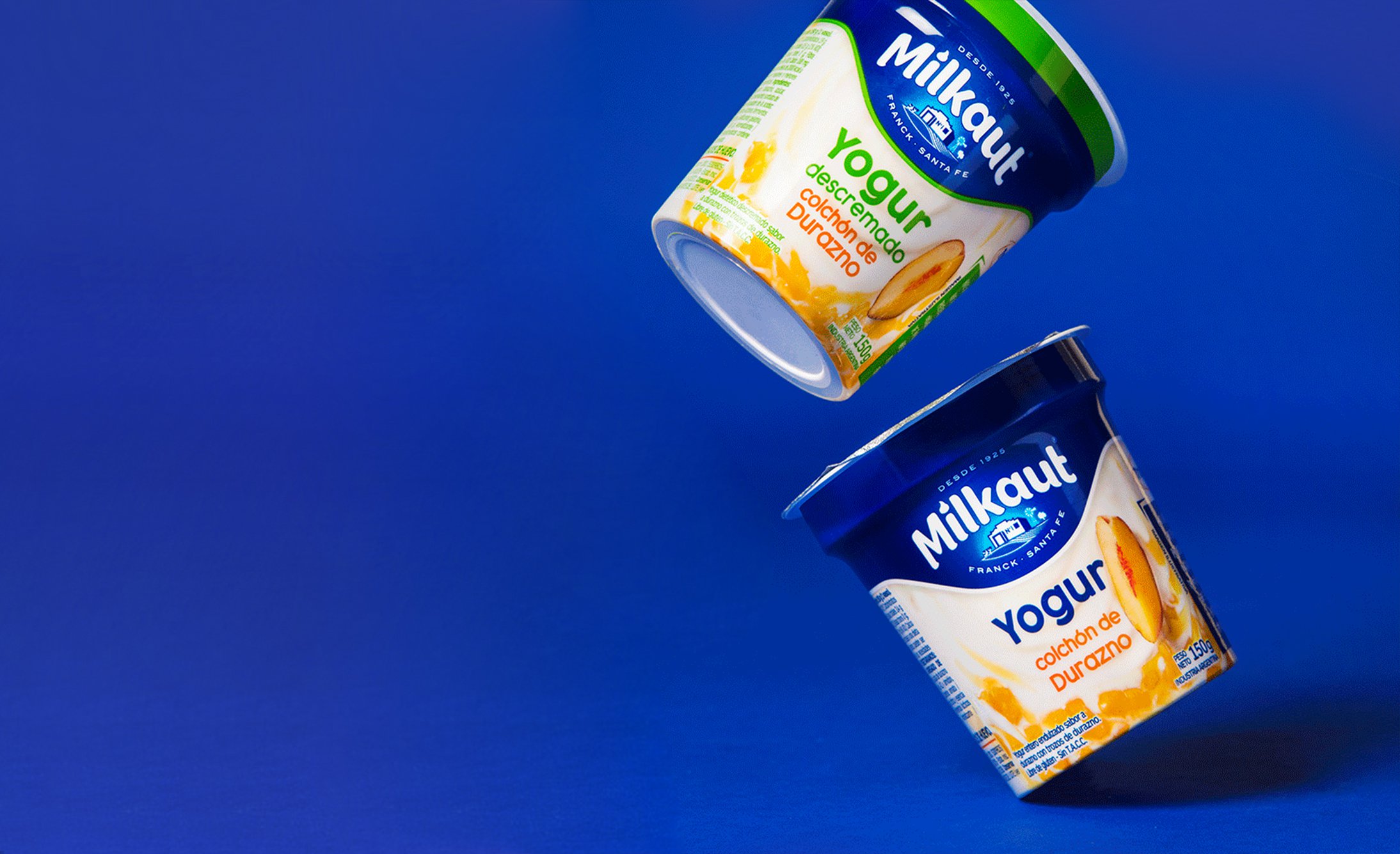 Dos tinas de yogur están flotando contra un fondo azul, mostrando un empaque colorido.