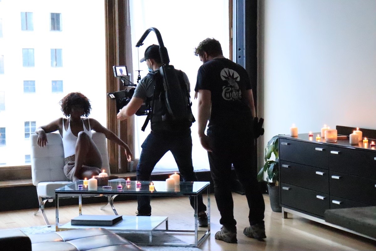 Cooper Ulrich, Director of Photography, filming Natasha Ofili as Amara/Sade (a dark-skinned Black woman sitting in a well-lit room with candles.