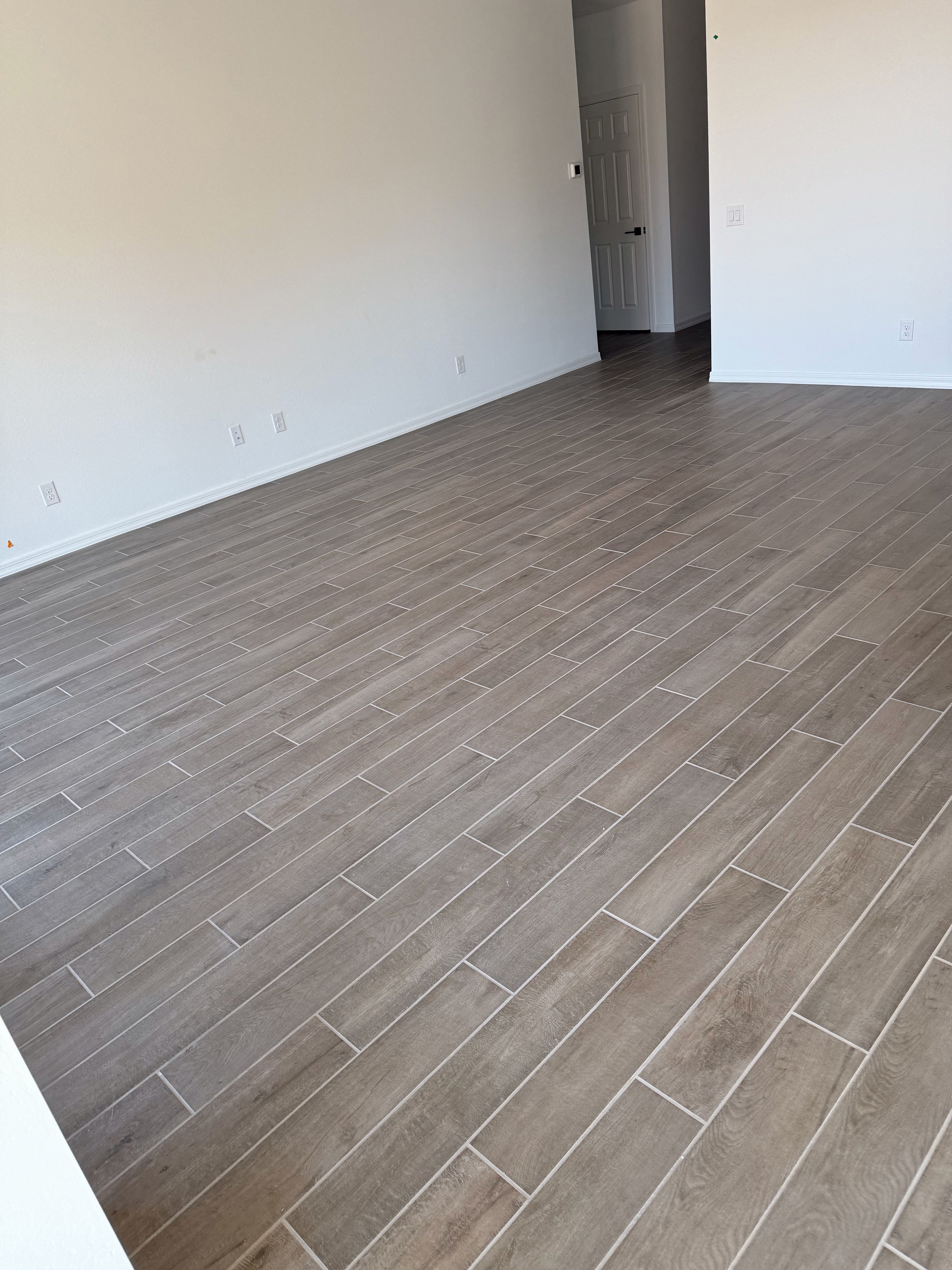 Modern open living area with wood-look tile flooring, white walls, and natural light in a new home under construction.
