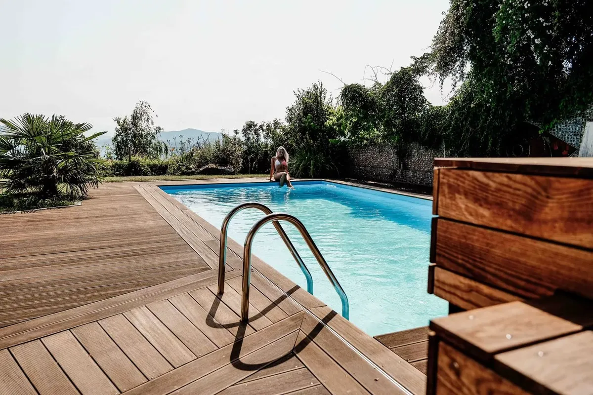 Poolleiter und Holzdeck im Sonnenlicht, dahinter der Garten mit Blick über das Tal