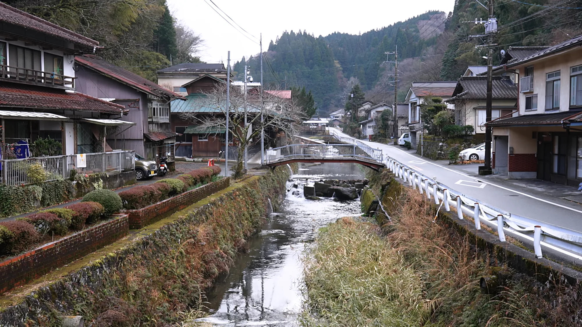 Roadside houses along a channelled stream near Kurokawa Onsen, hills behind