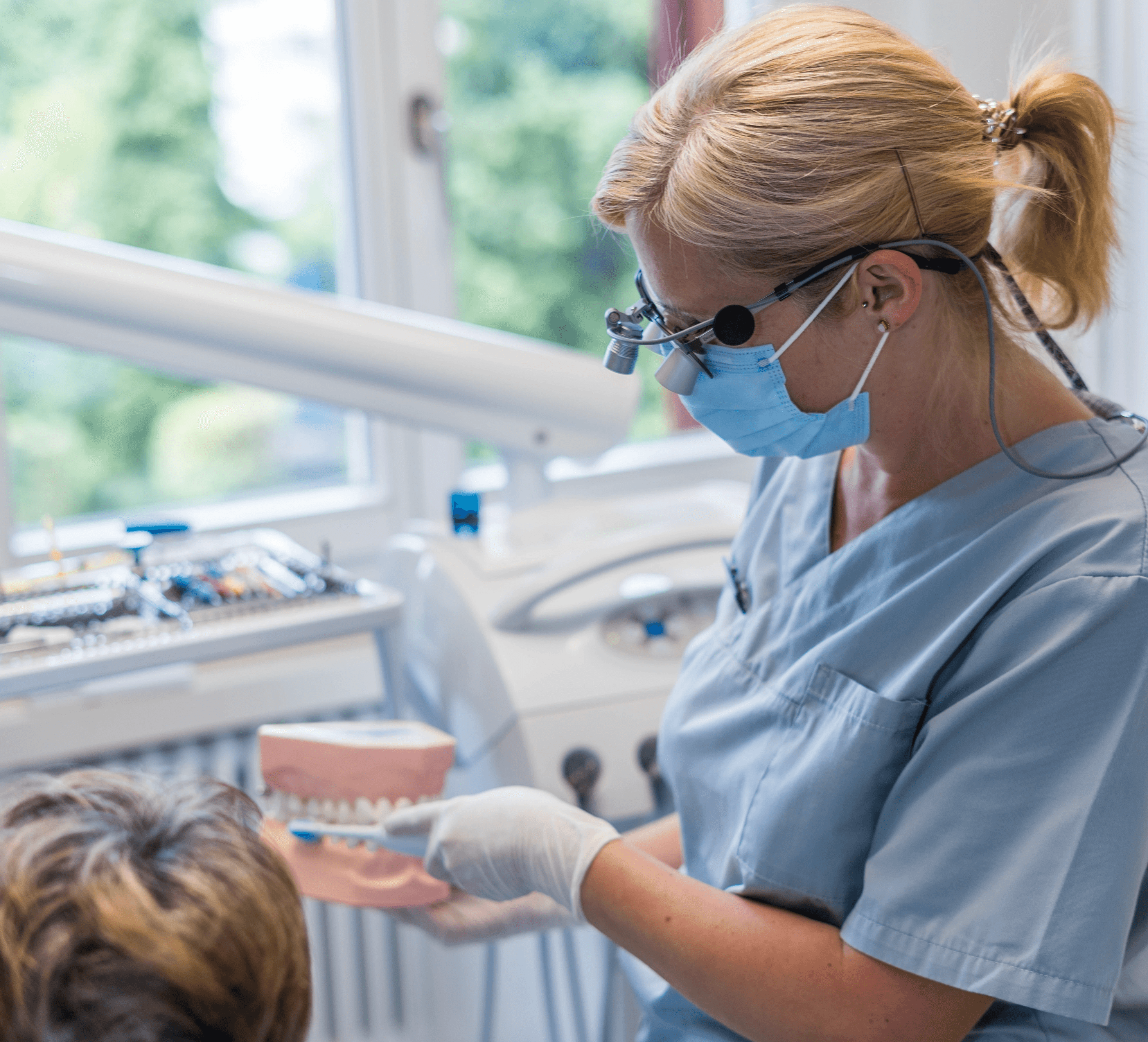 Dentalhygienikerin mit Lupenbrille erklärt anhand eines Zahnmodells die richtige Zahnpflege in einer Praxis.