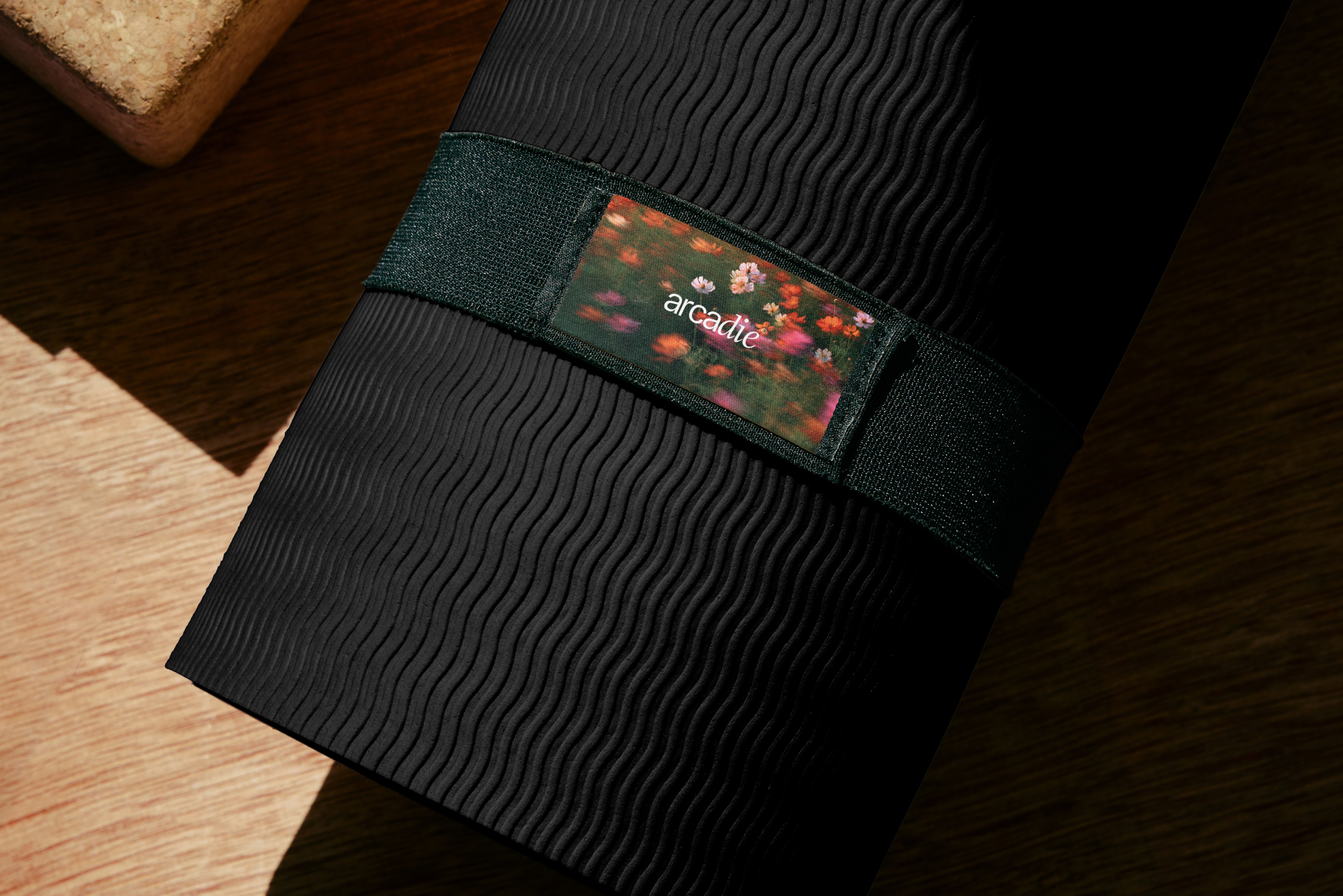 Tapis de yoga noir haut de gamme avec sangle verte et étiquette florale arcadie, identité visuelle pour marque de bien-être.