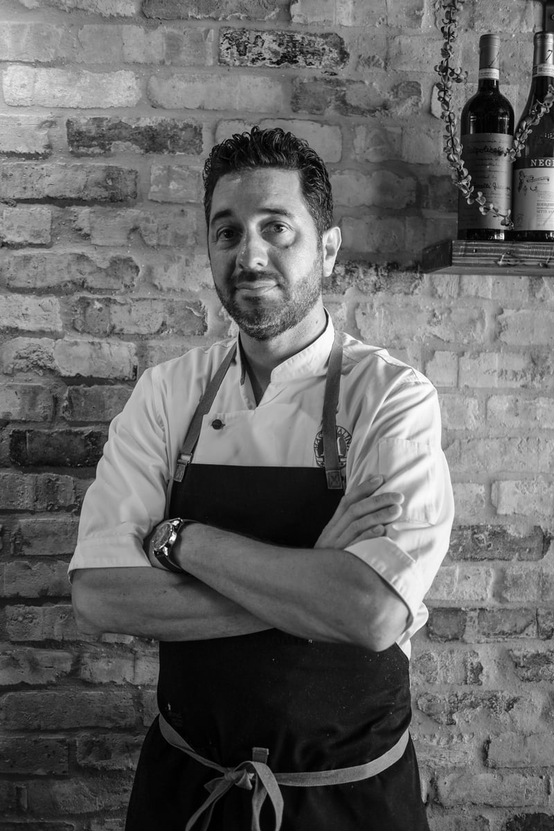 Chef Mike of Macchialina standing confidently with arms crossed in front of a brick wall.