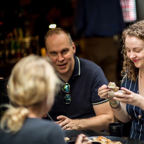 三个人坐在灯光昏暗的餐厅的一张桌子旁，边吃边聊天。重点在于坐在中间的那位男士。