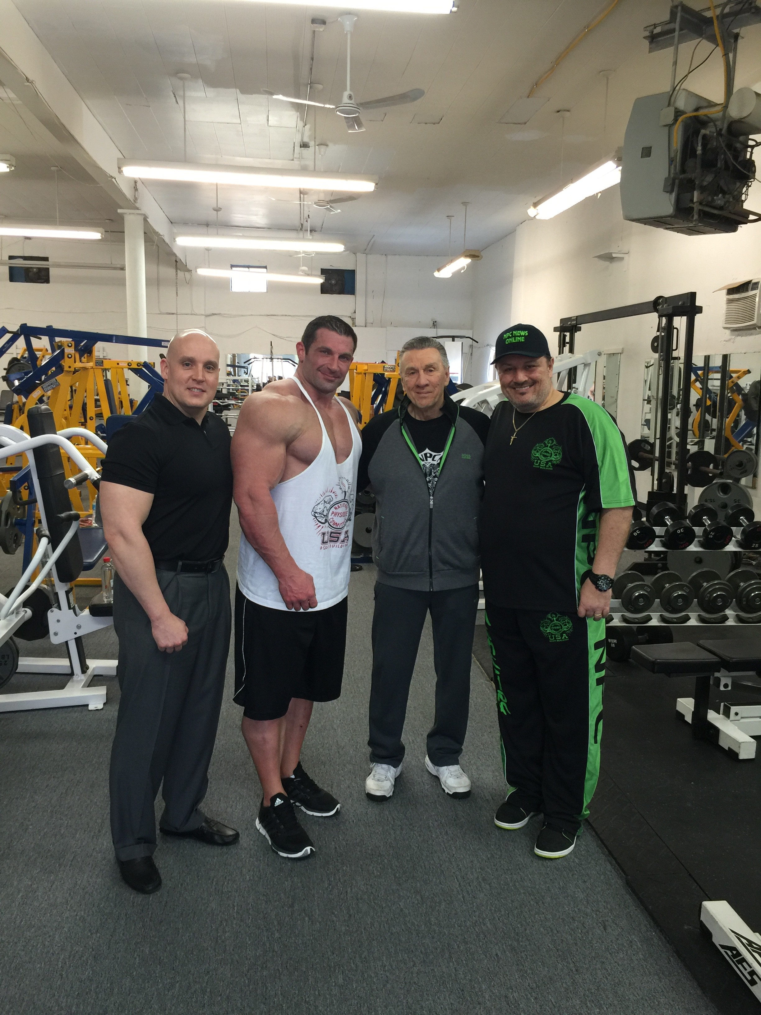 Four men posing on the gym floor among weight machines and dumbbell racks