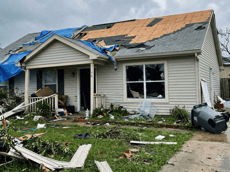 House with damaged roof, broken window, and debris