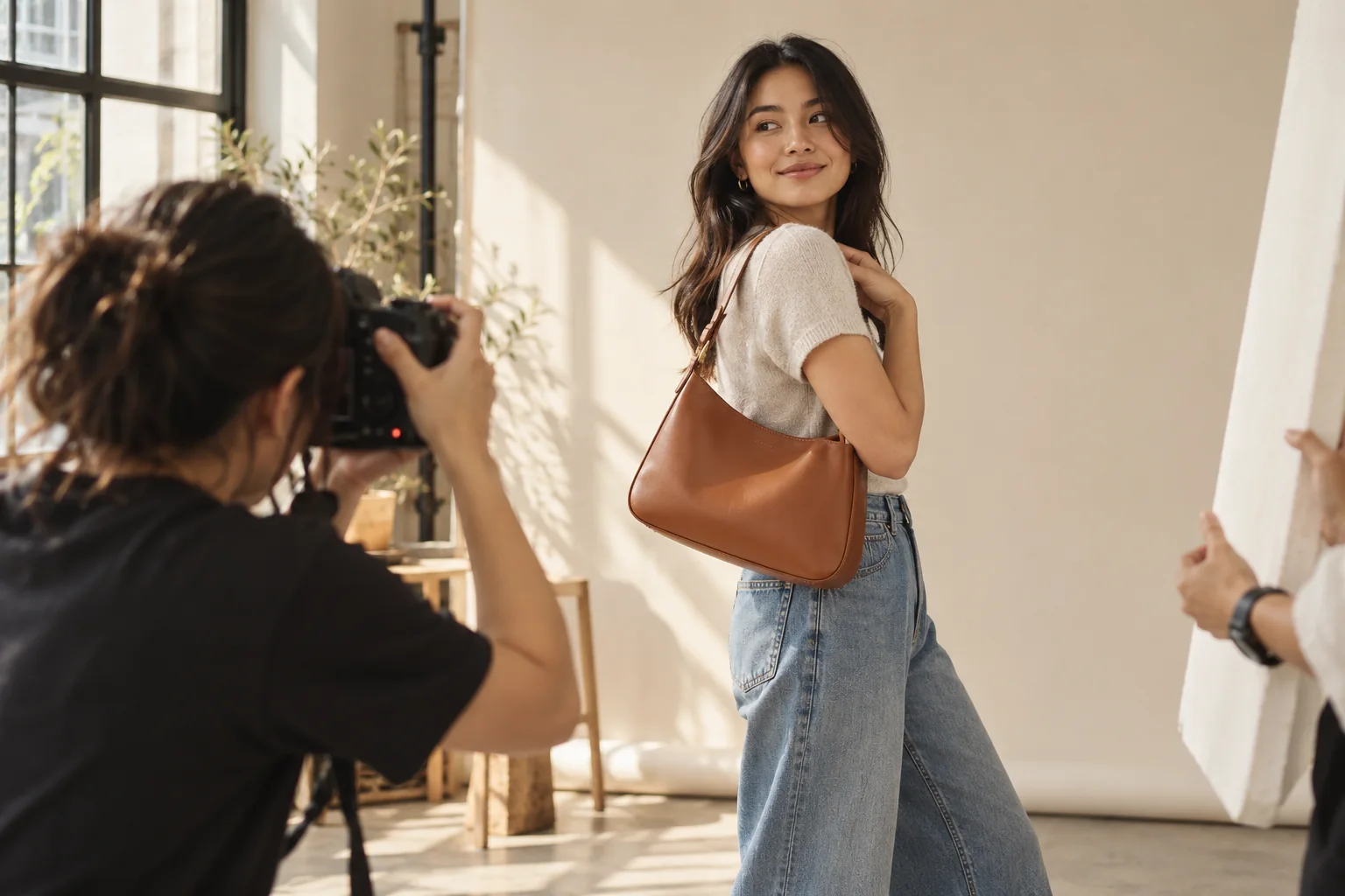Photographer capturing a lifestyle model wearing a caramel shoulder bag in a sunlit studio