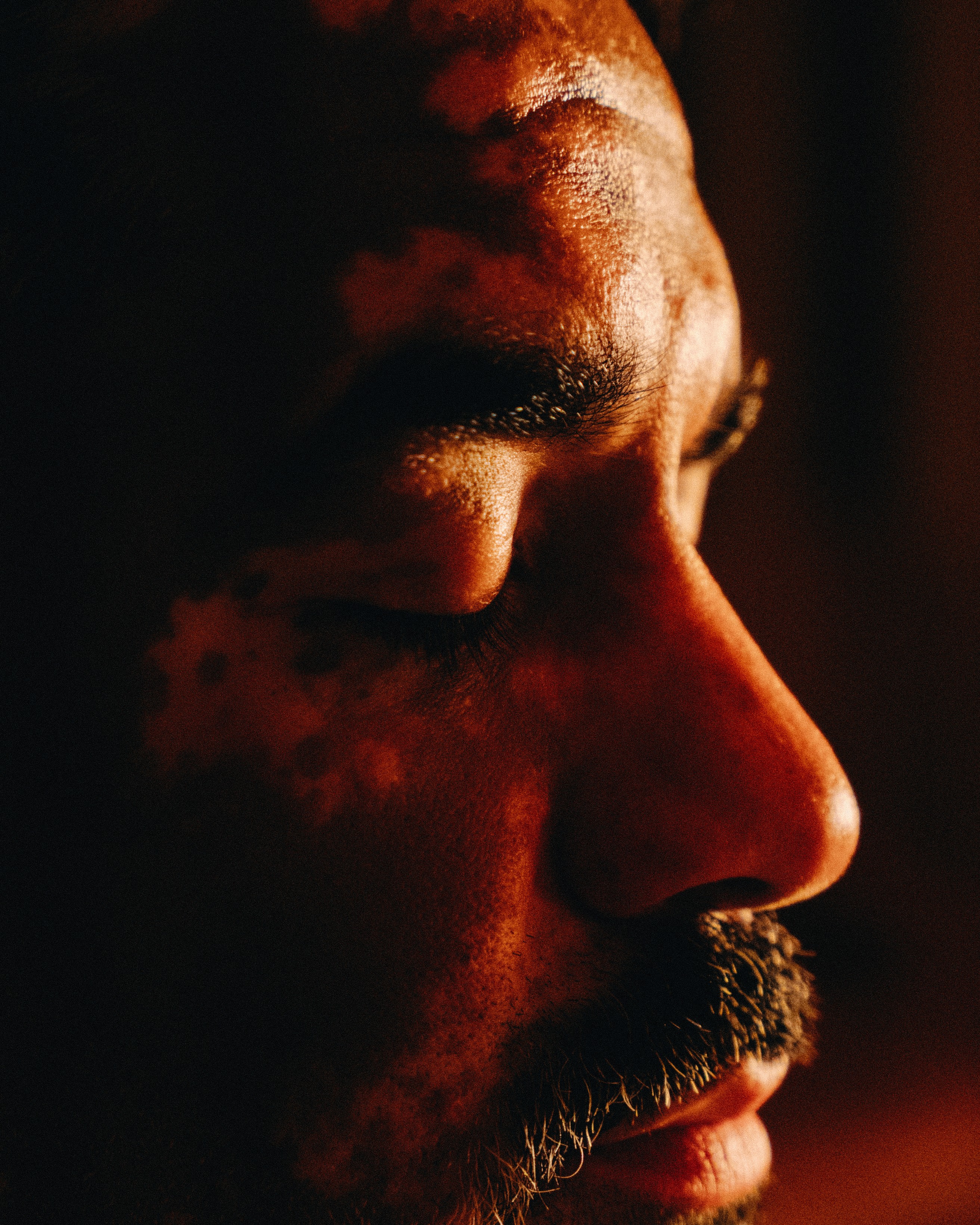 Close-up profile of a person breathing slowly in a dim sauna, eyes lowered in quiet reflection during a silent session