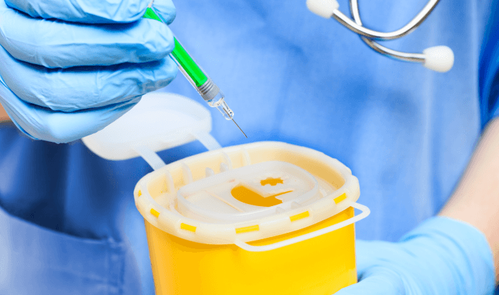 Healthcare worker holding syringe over medical sharps container.