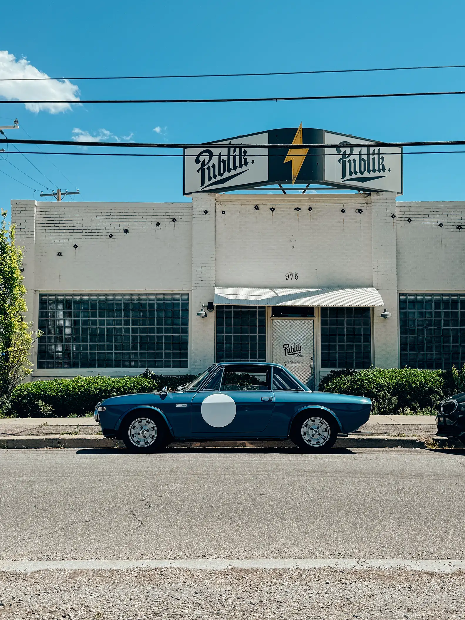 A blue Lancia Fulvia sports car parked in front of a building.