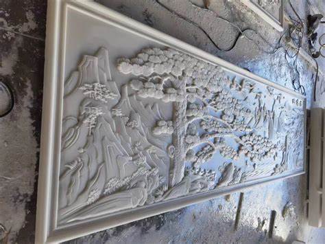 A white stone relief panel in progress, featuring delicate carvings of trees and mountains in a traditional Chinese style.