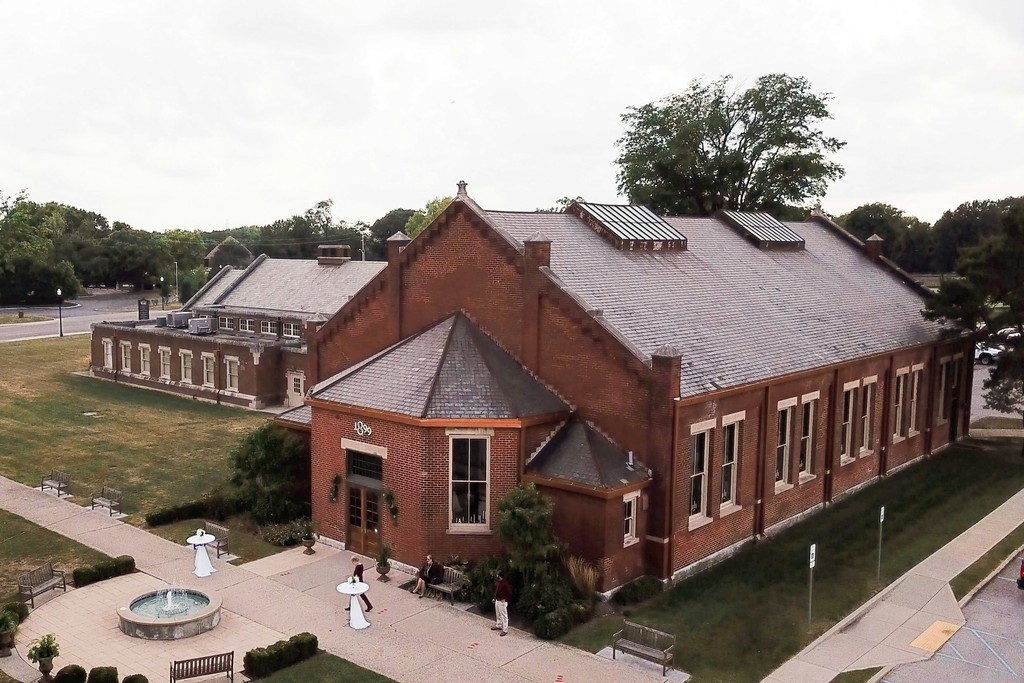 Aerial view of a historic red brick wedding venue with slate roofing, a courtyard fountain, and manicured green lawn