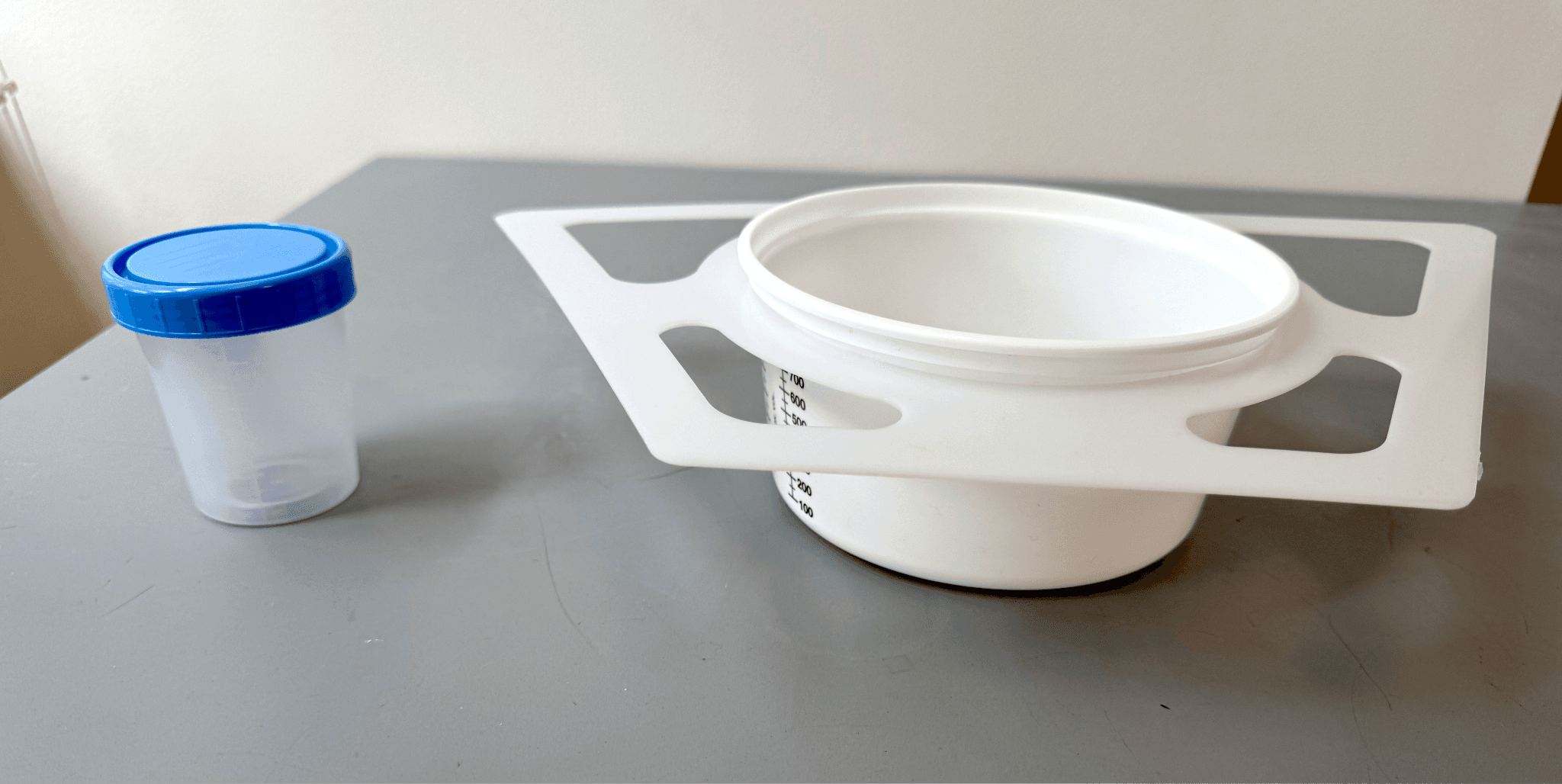 A small specimen sample cup next to a poop collection device that resembles a cool whip tub with plastic wings.
