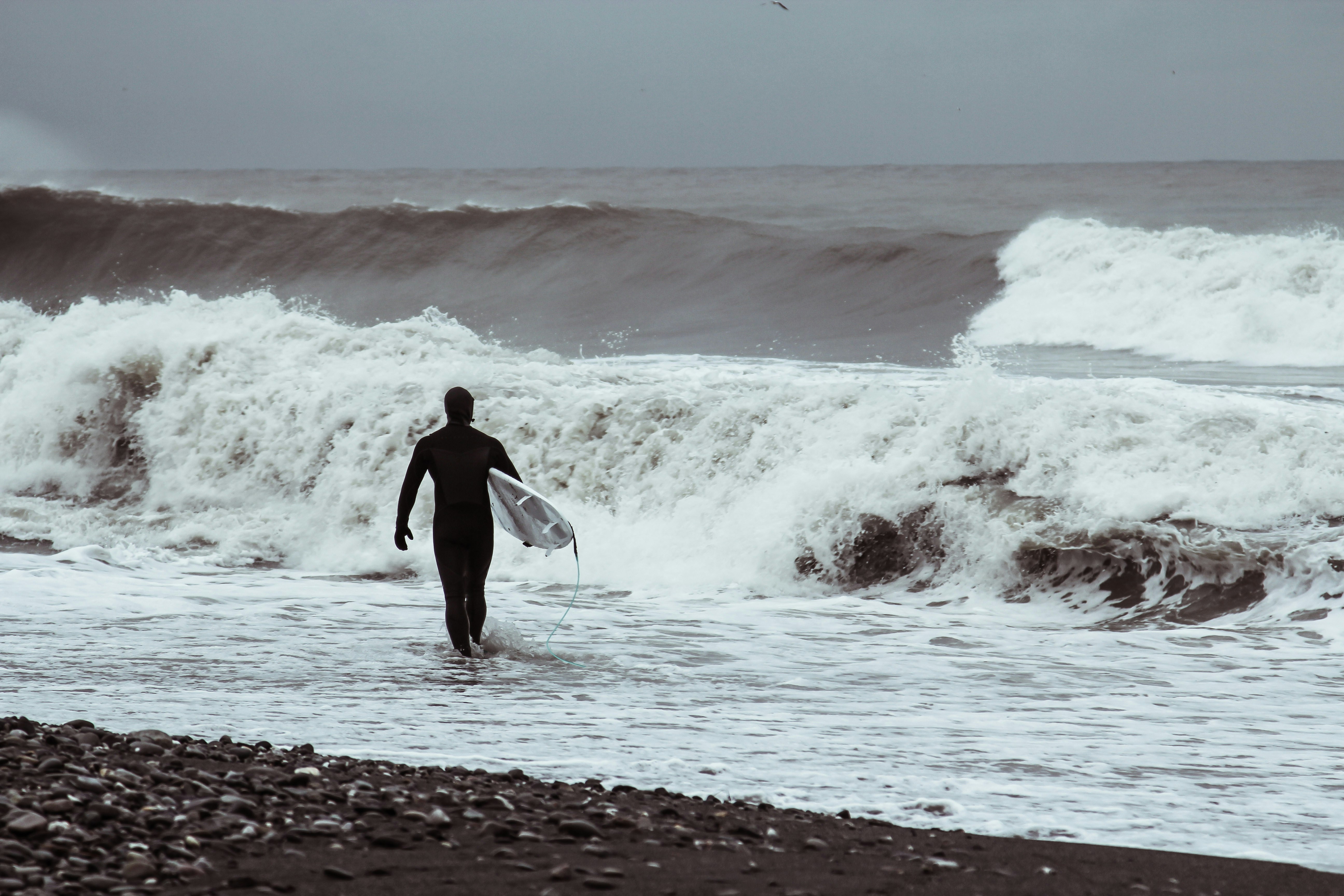 Surfer preparing to enter the water on a black sand beach.