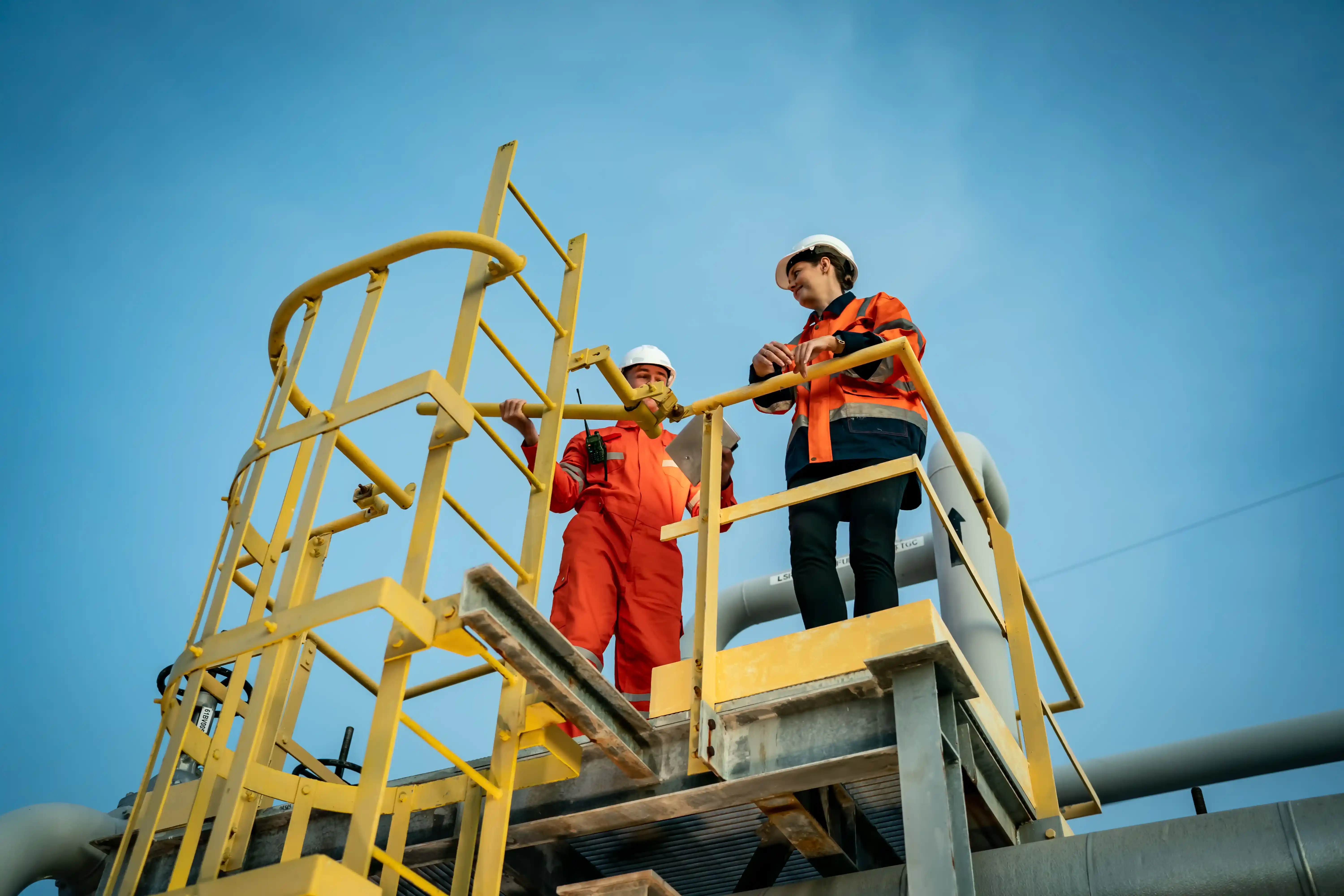 Workers installing safety platform and ladder on industrial equipment