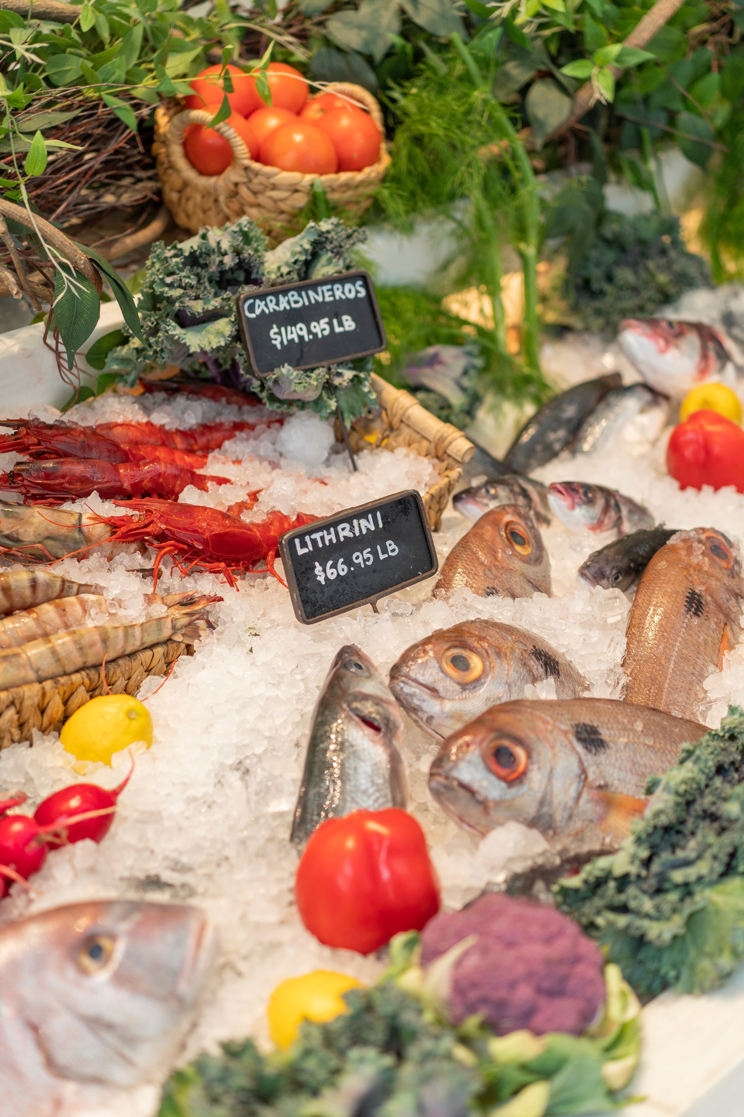 A colorful display of fresh vegetables, herbs, and fruits arranged on a table with small labels.