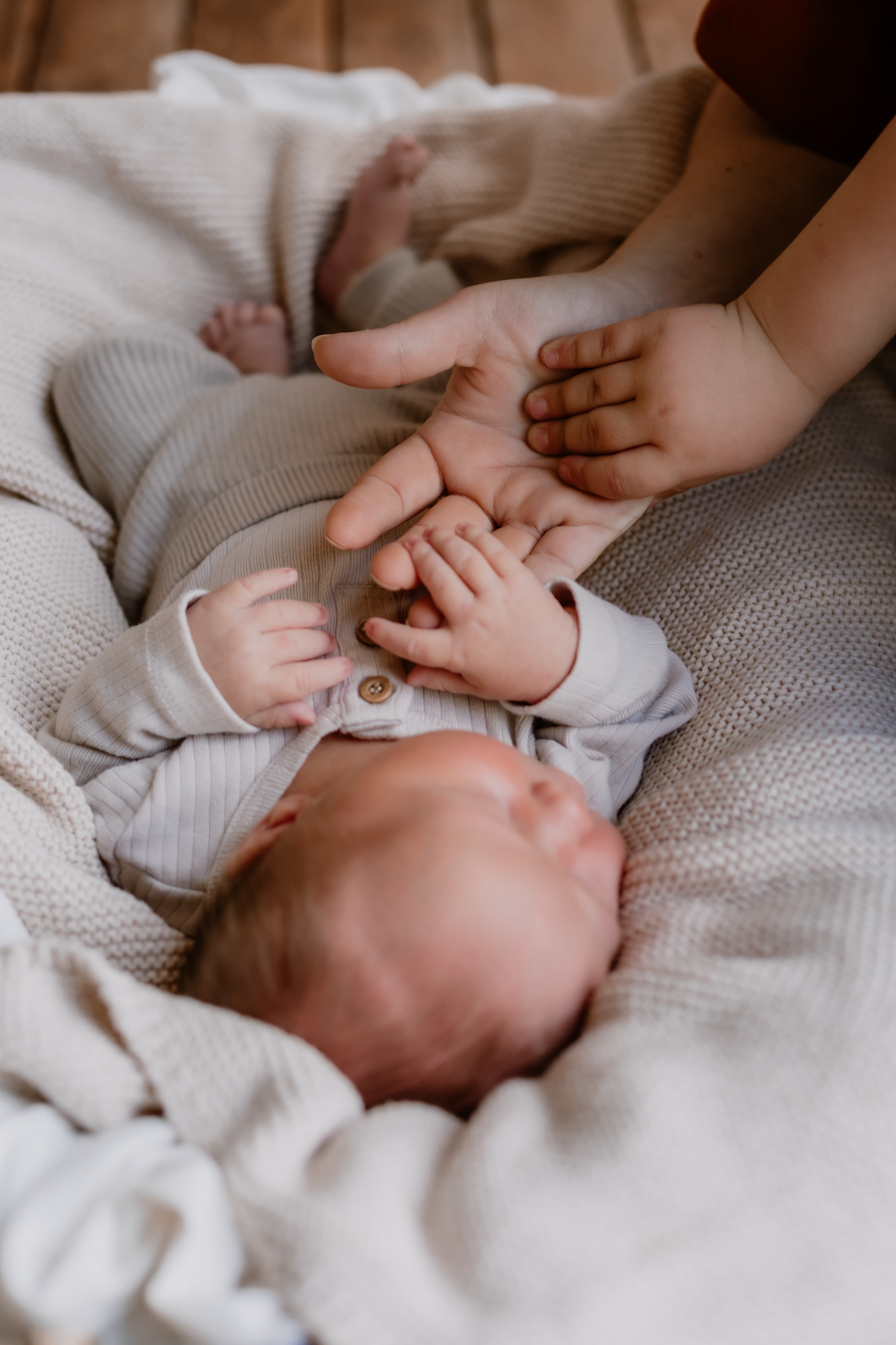 Parent and siblings holding newborn baby's hand while sleeping in a basket in newborn baby photoshoot Mackay