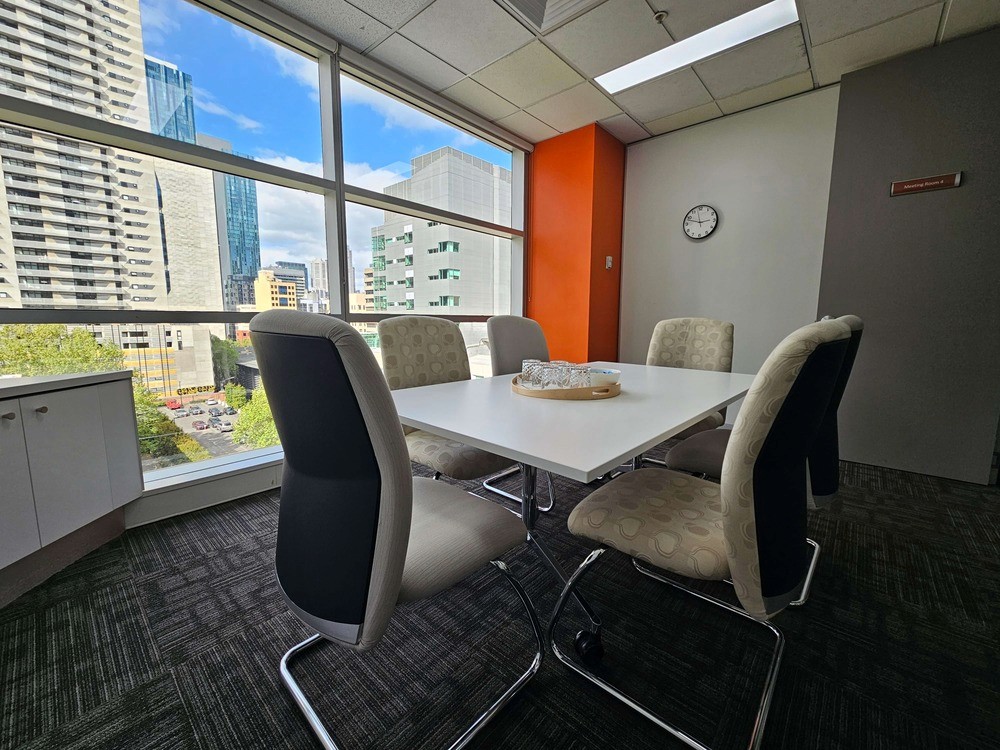 A confidential, secure room for mediation services, featuring six chairs, a table and a large window with a cityscape view.