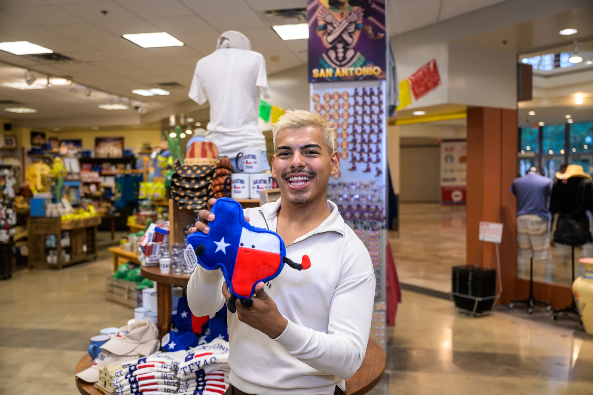 Shopper holding a Texas-flag plush souvenir inside the Life in Alamo City gift shop