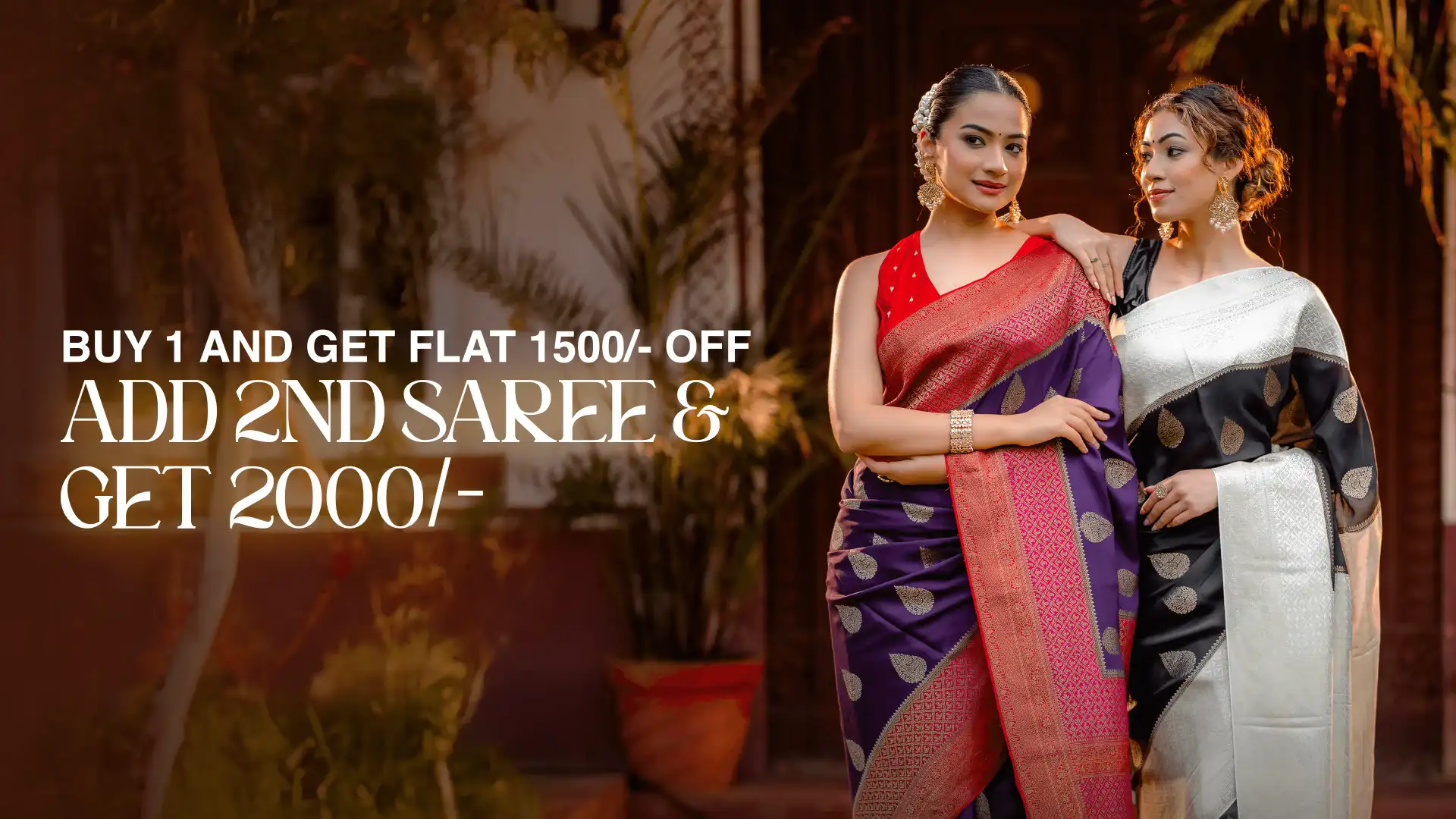 Two women standing together—one wearing a purple crepe silk saree with a pink-red contrast border and zari buttas, and the other wearing a black and white crepe saree—showcasing elegant handcrafted designs from That Saree Shop.