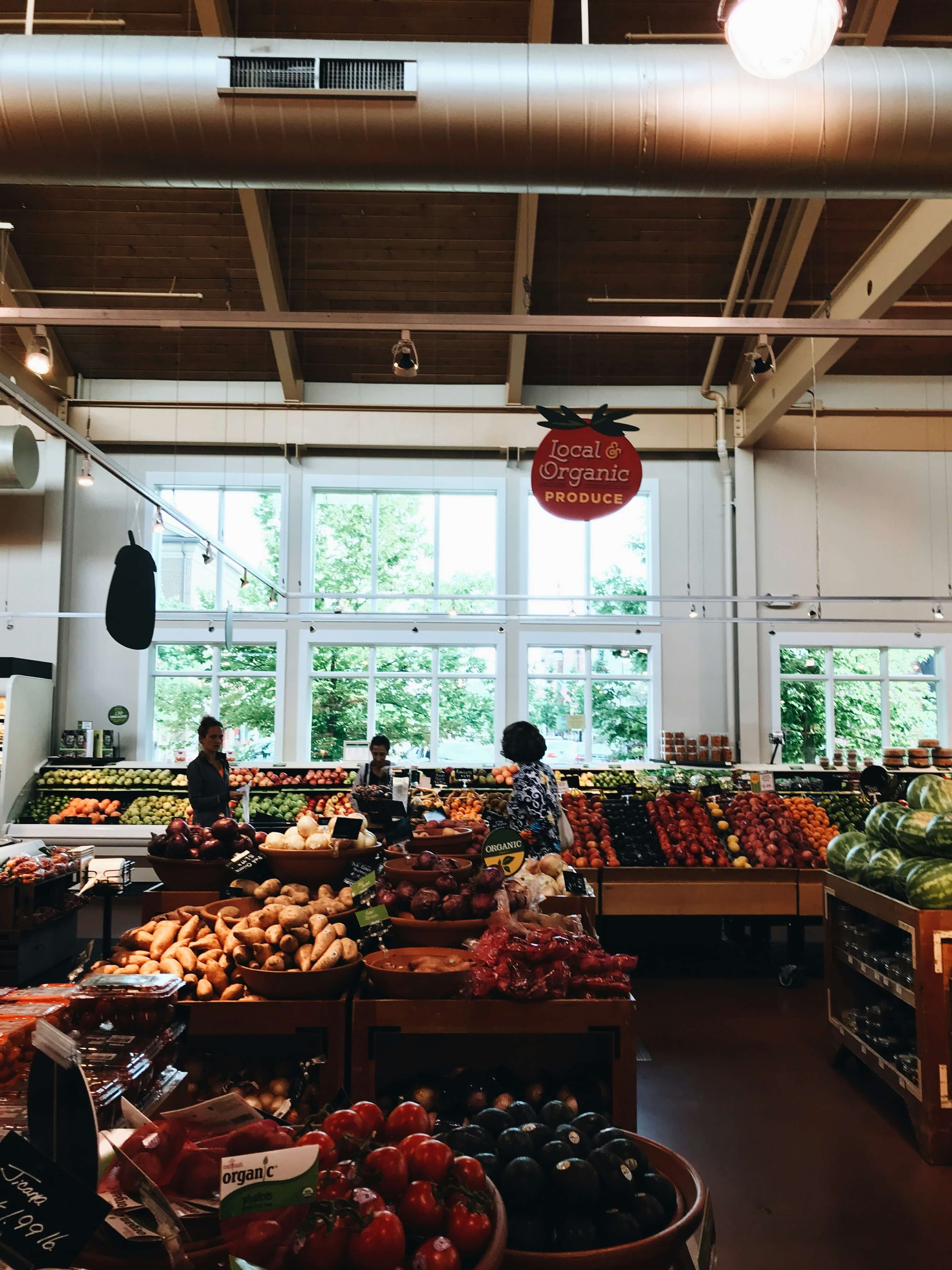Shoppers selecting fresh local and organic produce in a grocery store market.