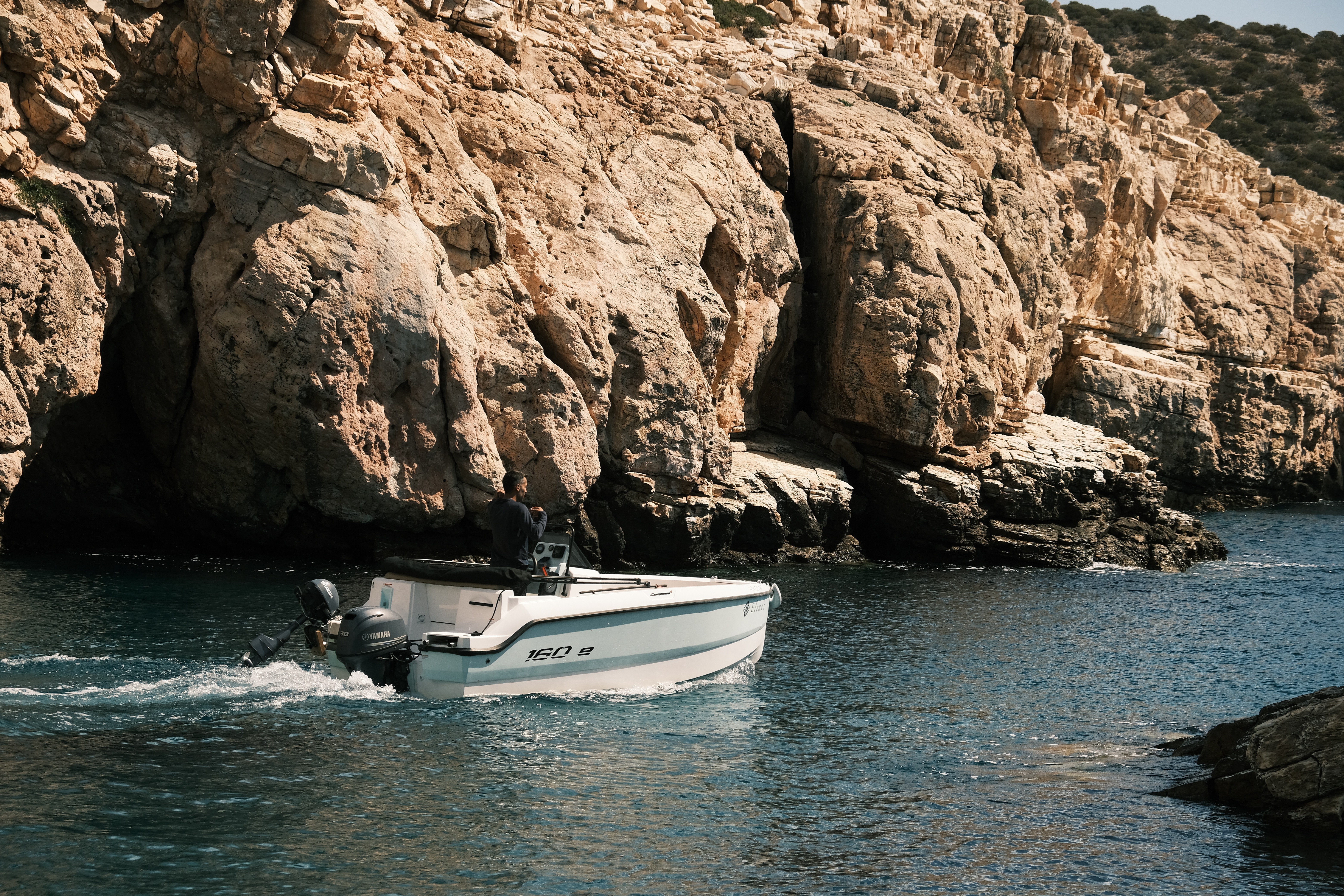 White Compass 16Oe yacht cruising through turquoise waters along dramatic limestone cliffs in the Cyclades.
