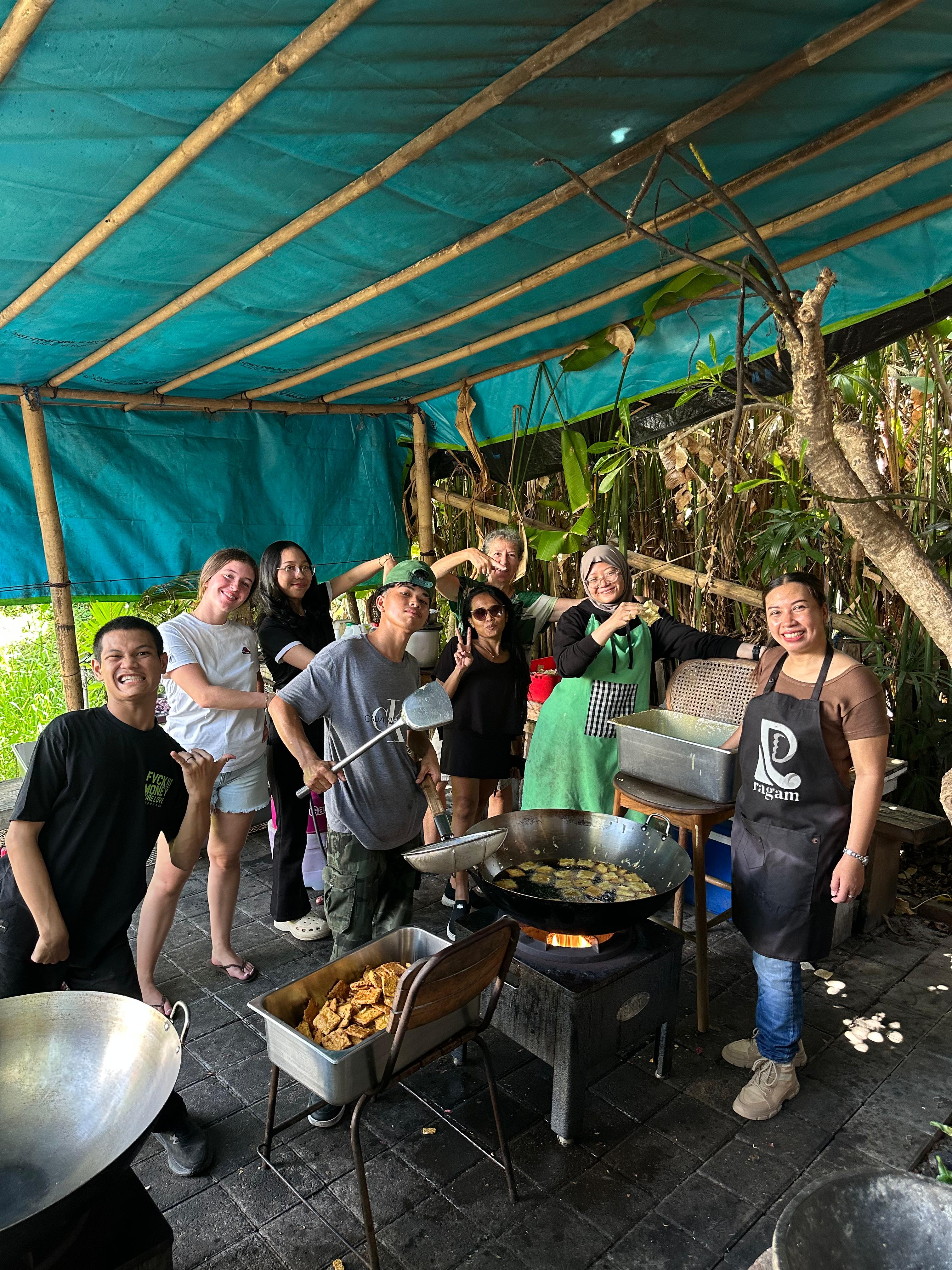 Ragam volunteer team stands behind trays of packed meals inside the community kitchen during a daily cooking shift in Bali.