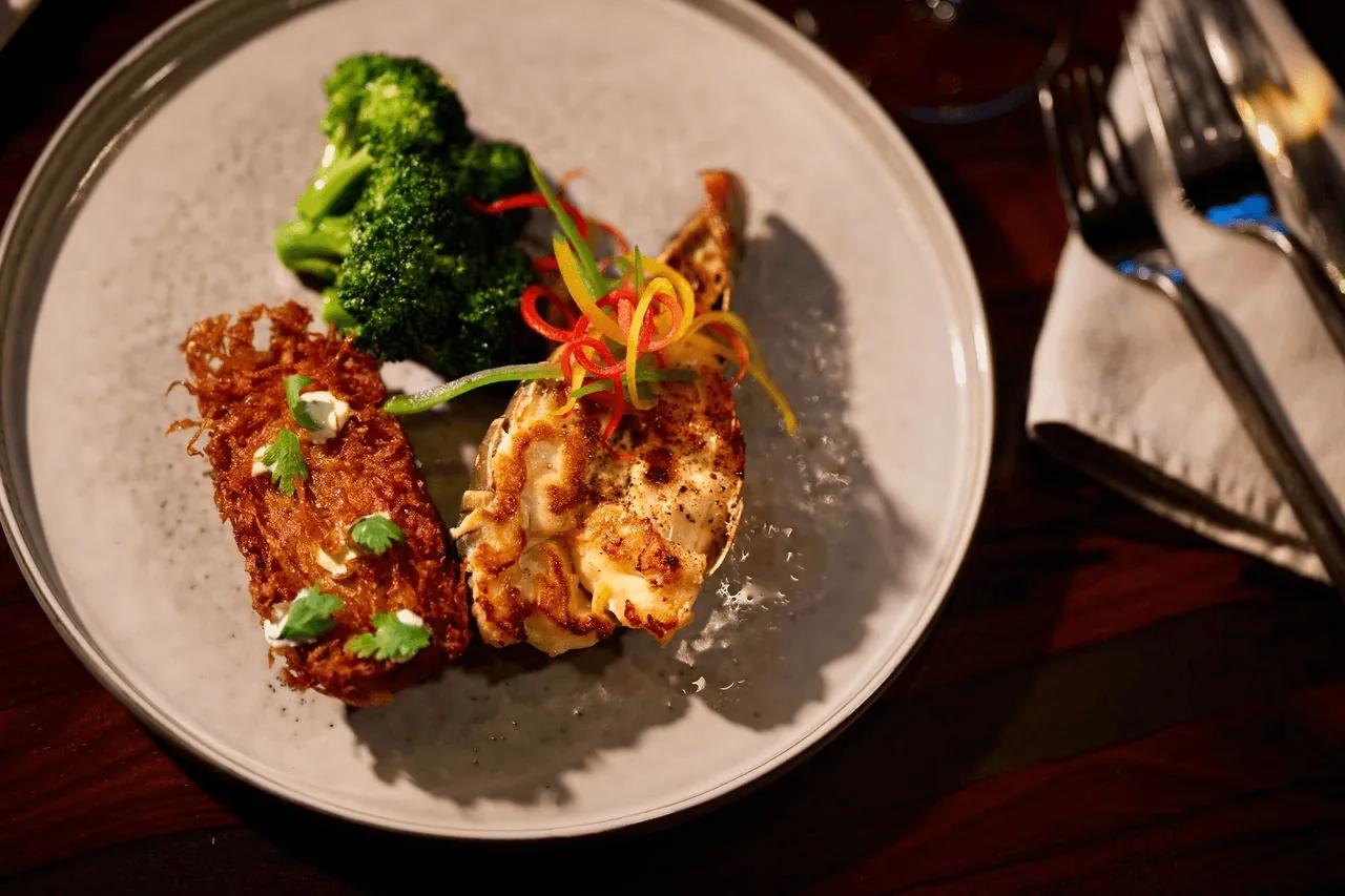 A plate of grilled chicken, brocoli and vegetables on a wooden table.
