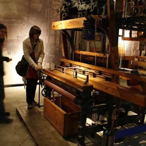 两个人在一个灯光昏暗的房间里操作一个大型木制织布机。