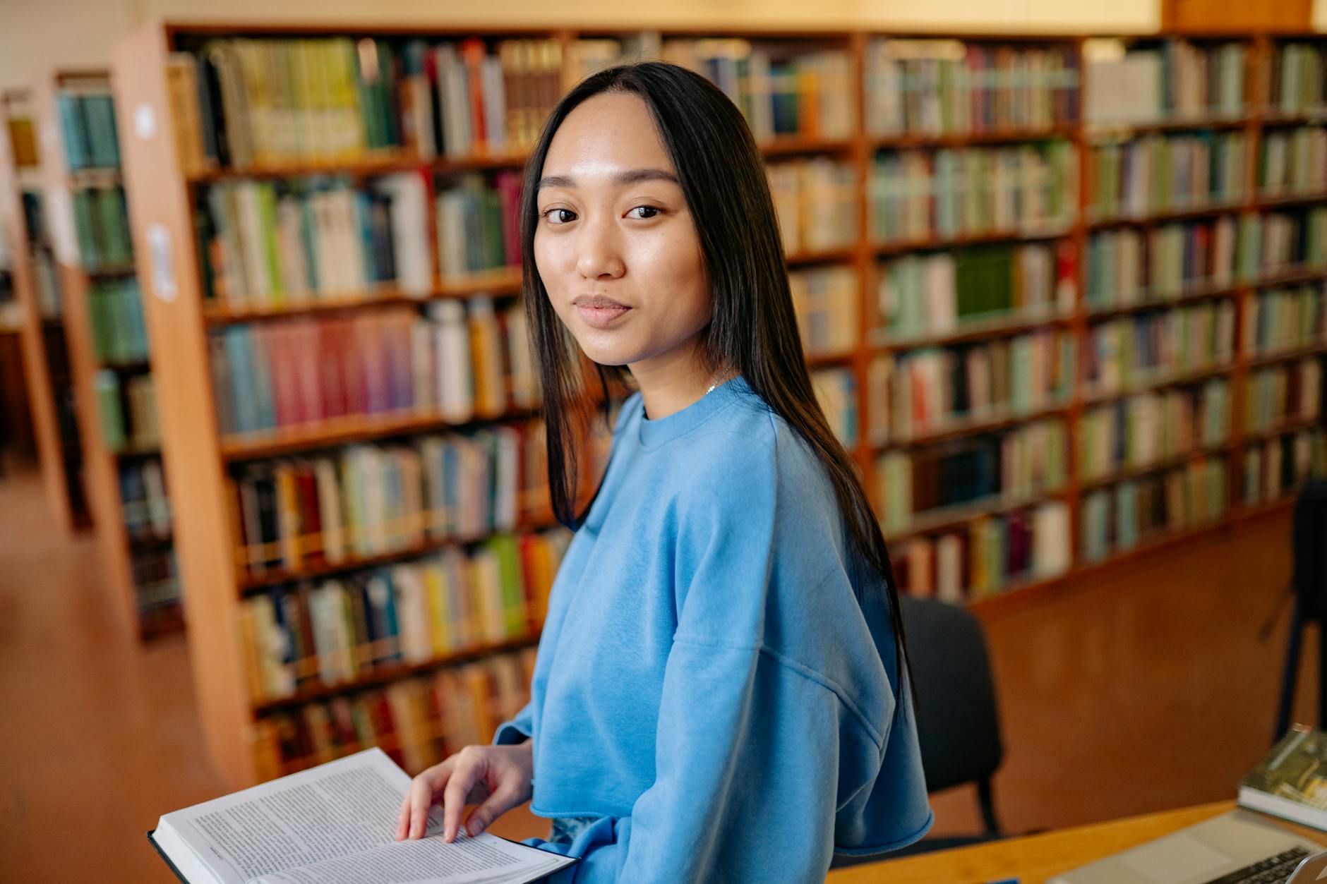 A focused student studying textbooks and a laptop in a quiet university library setting.