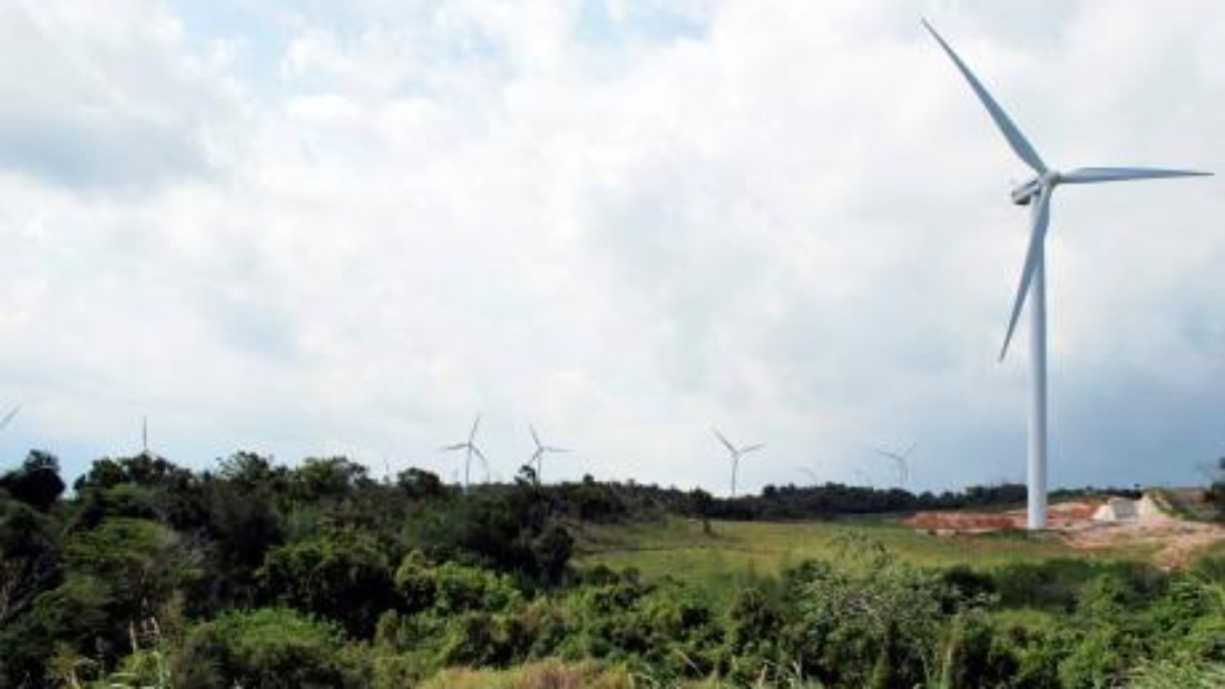 Wind turbine on a bushy hill with turbines further in the background