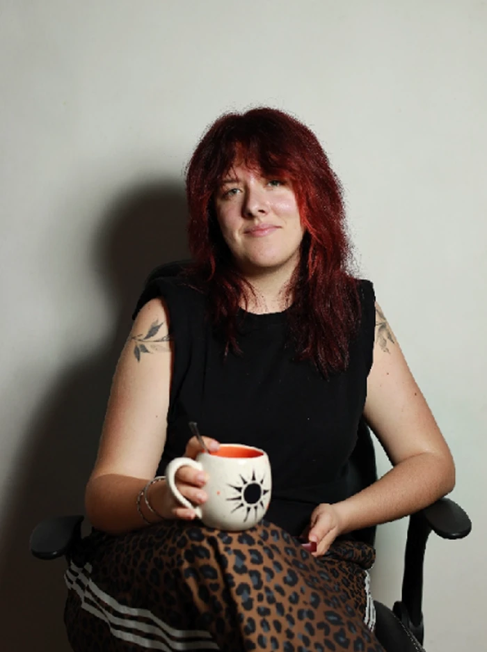 Maïlys Vial assise sur une chaise noire avec une tasse à la main.