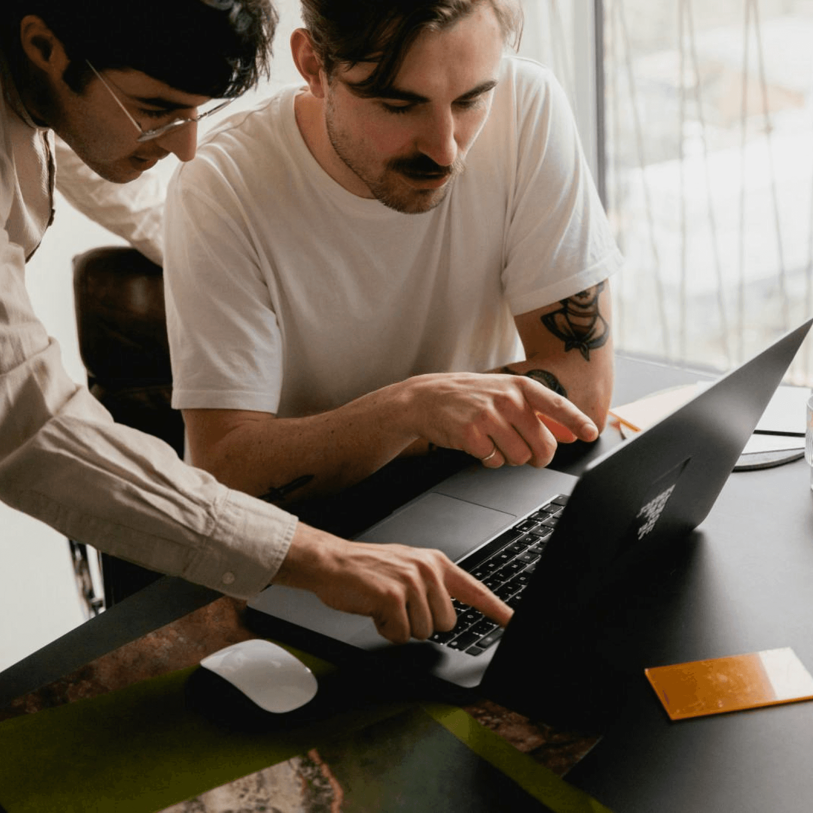 Two men collaborating on a laptop in a modern office setting, focused on their work and sharing ideas