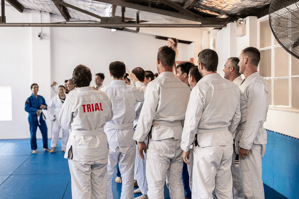 Group of new students wearing white gis, one marked "TRIAL", listening to an instructor at Gracie Sydney