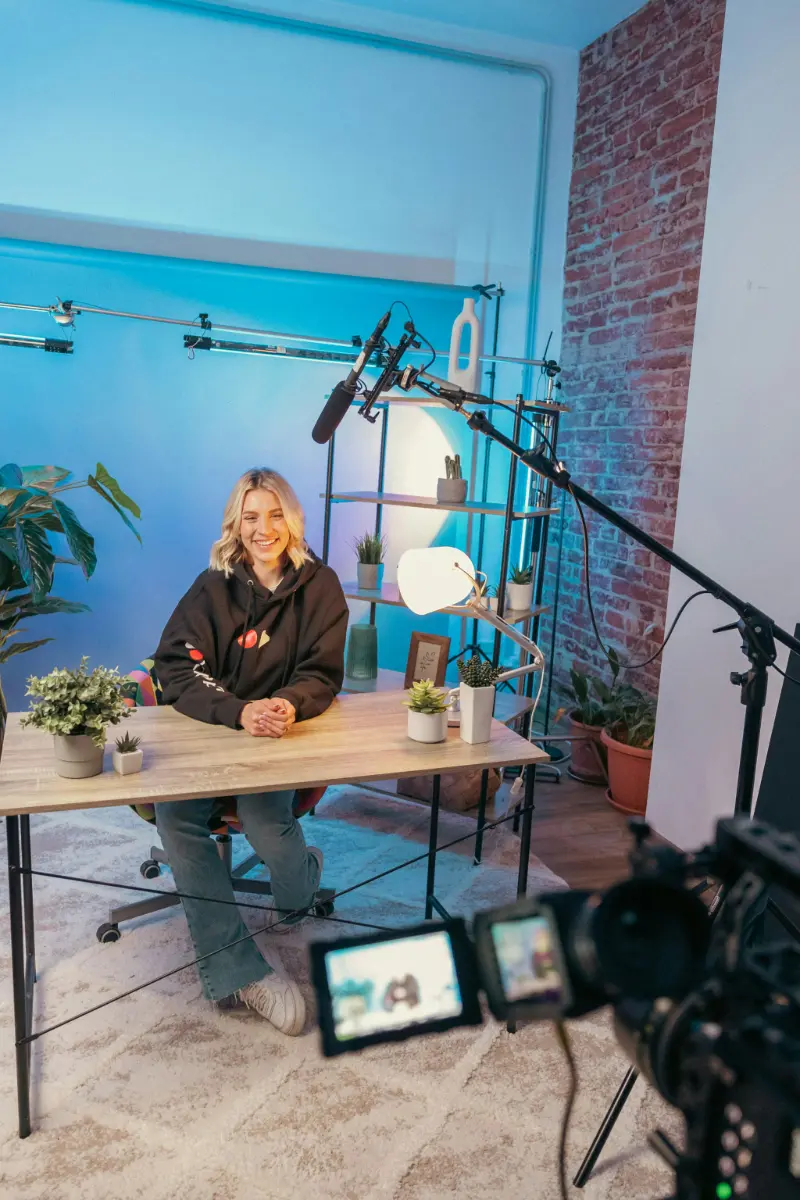 Content Marketing, lächelnde Frau in Podcastsetup mit einem Schreibtisch, Mikrofon und einem blauen Hintergrund.