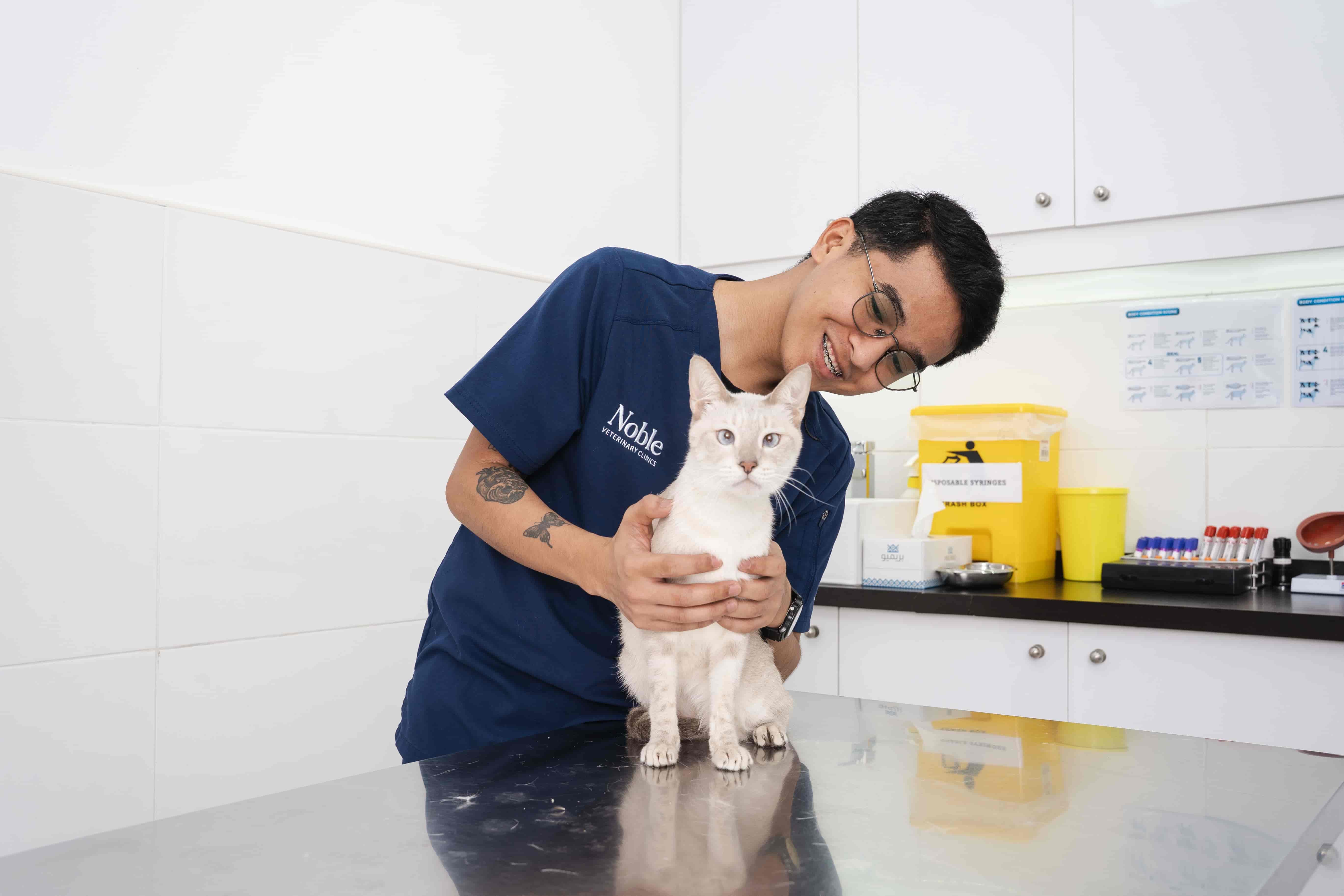 A veterinarian is smiling and holding a cat on a table. 