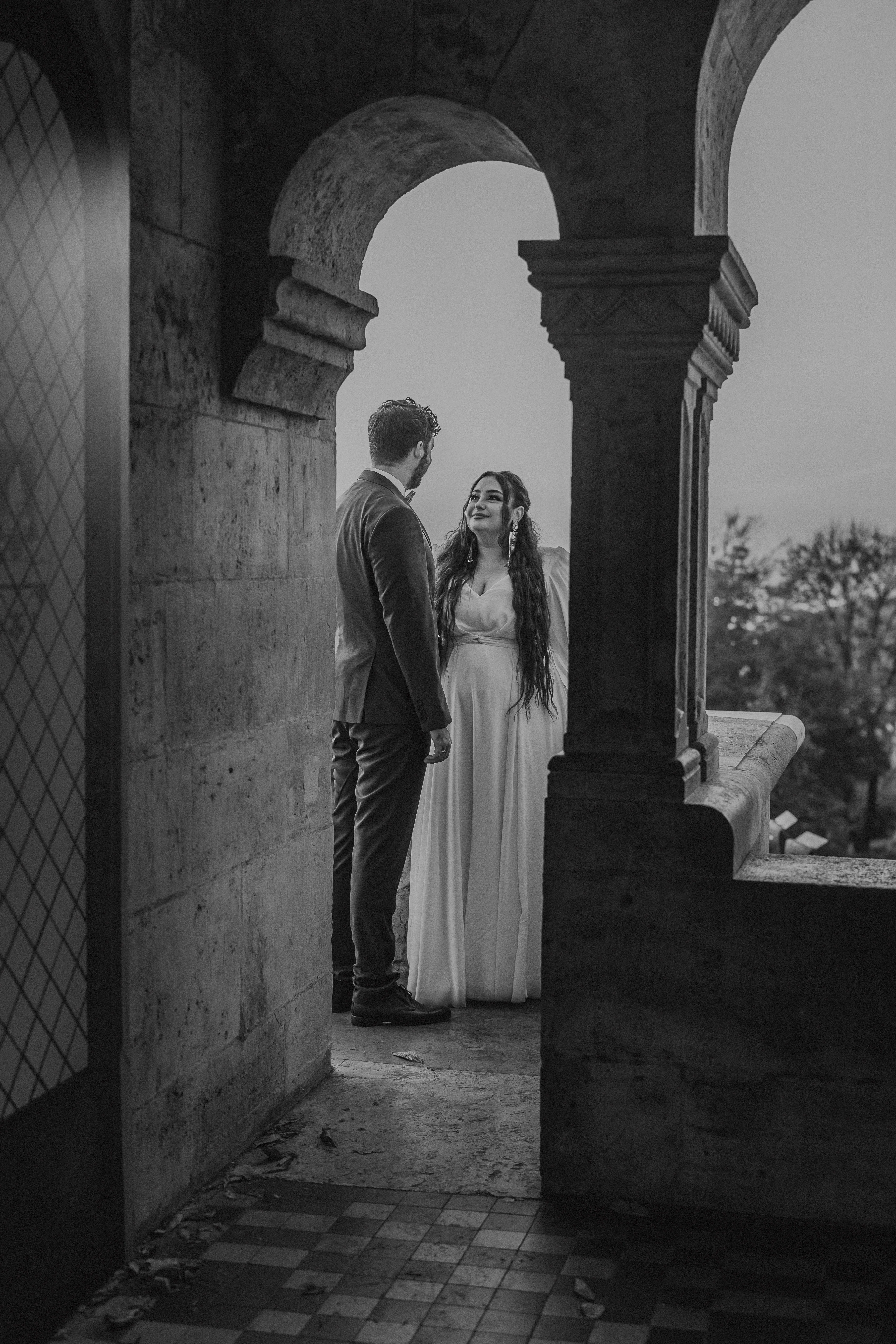 Fekete-fehér esküvői fotó menyasszonyról és vőlegényről román stílusú ívek között a budapesti Halászbástyán, terasz kilátással