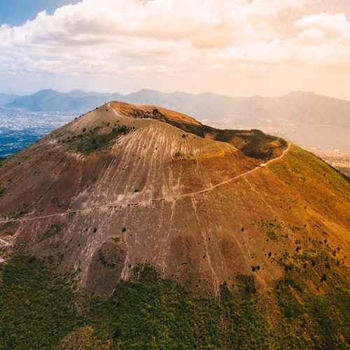 Aerial view of a mountainous landscape with a prominent peak, surrounded by green forest and distant hazy mountains.