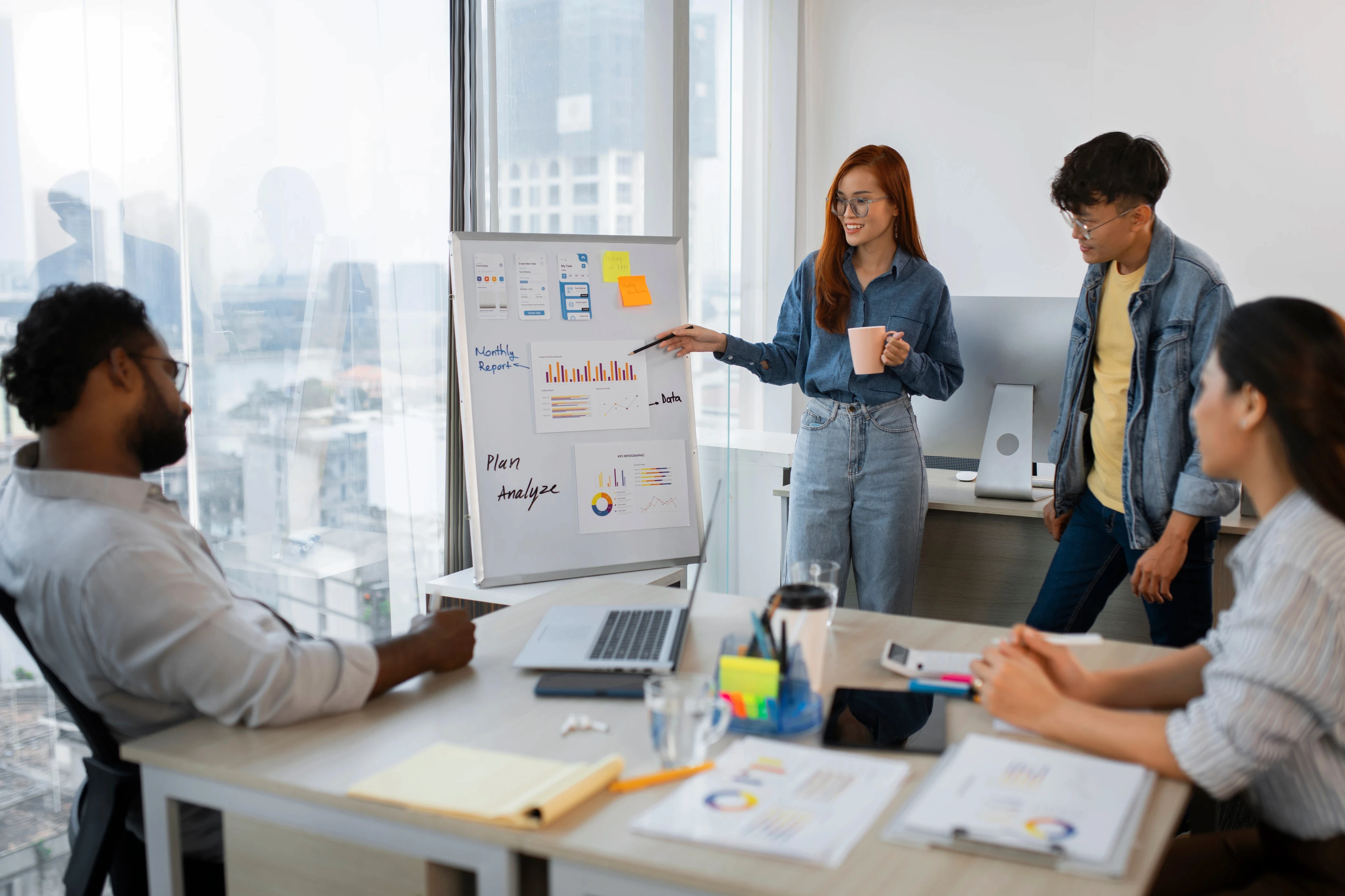 Team in a modern office reviewing charts and graphs on a whiteboard during a business presentation meeting.
