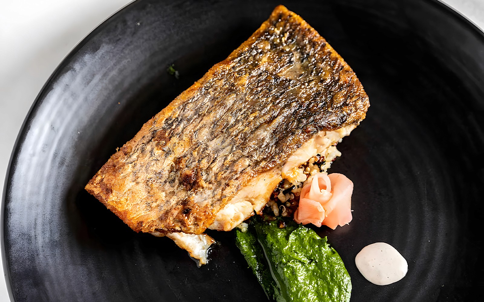 Gegrilde vis met quinoa, spinaziepuree en ingelegde gember op een zwart bord, Starlight Dinner Cruise Sydney.