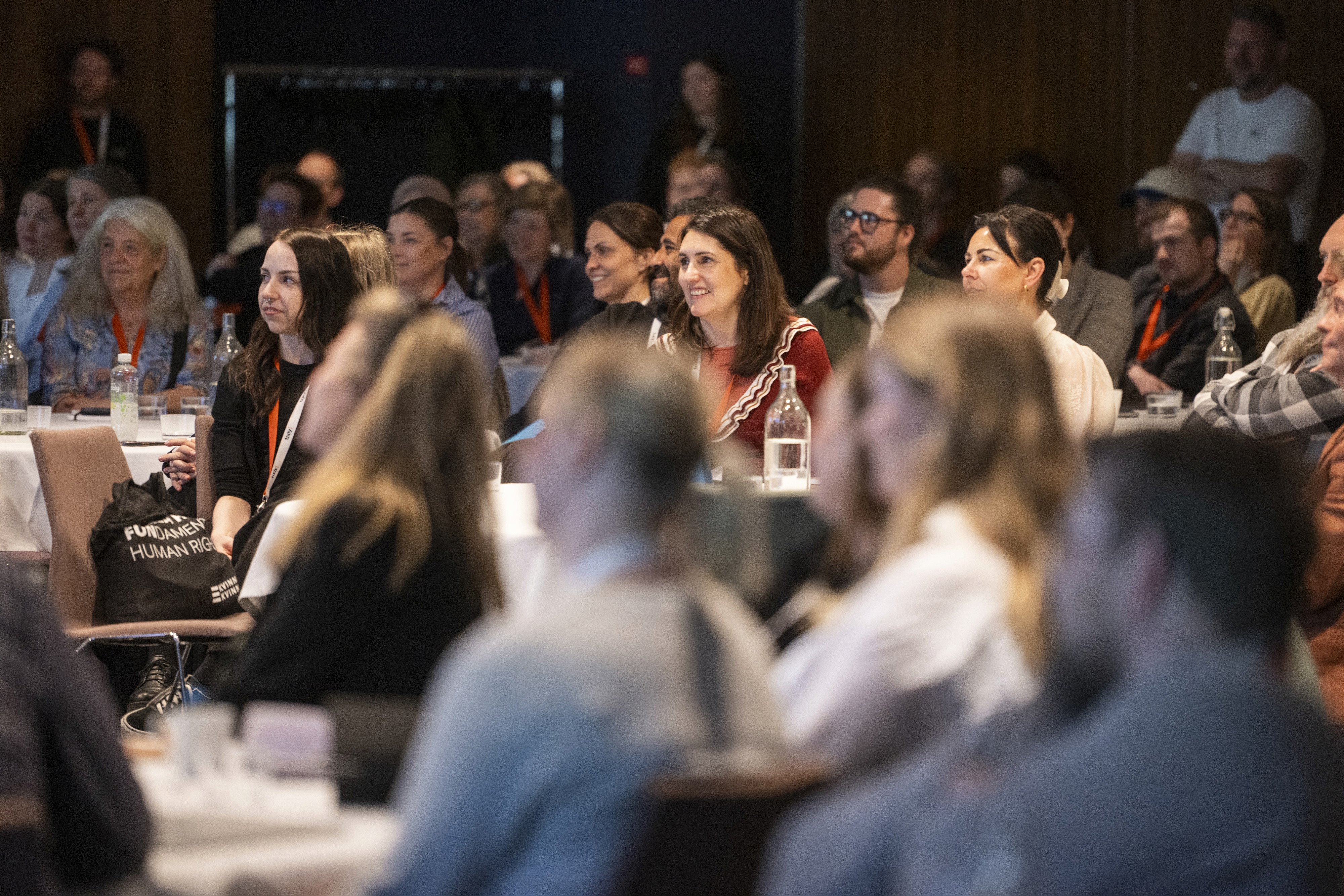 A group of people engaged in discussion at a conference or meeting, seated around tables.