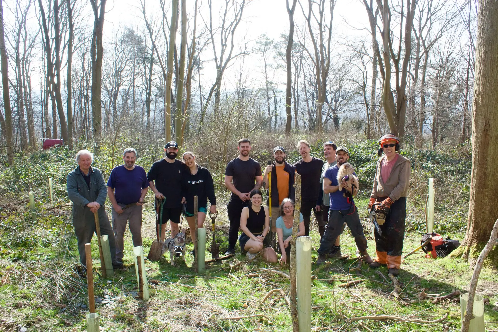 A group of people gathered in a forest, smiling and posing together amidst trees and greenery.