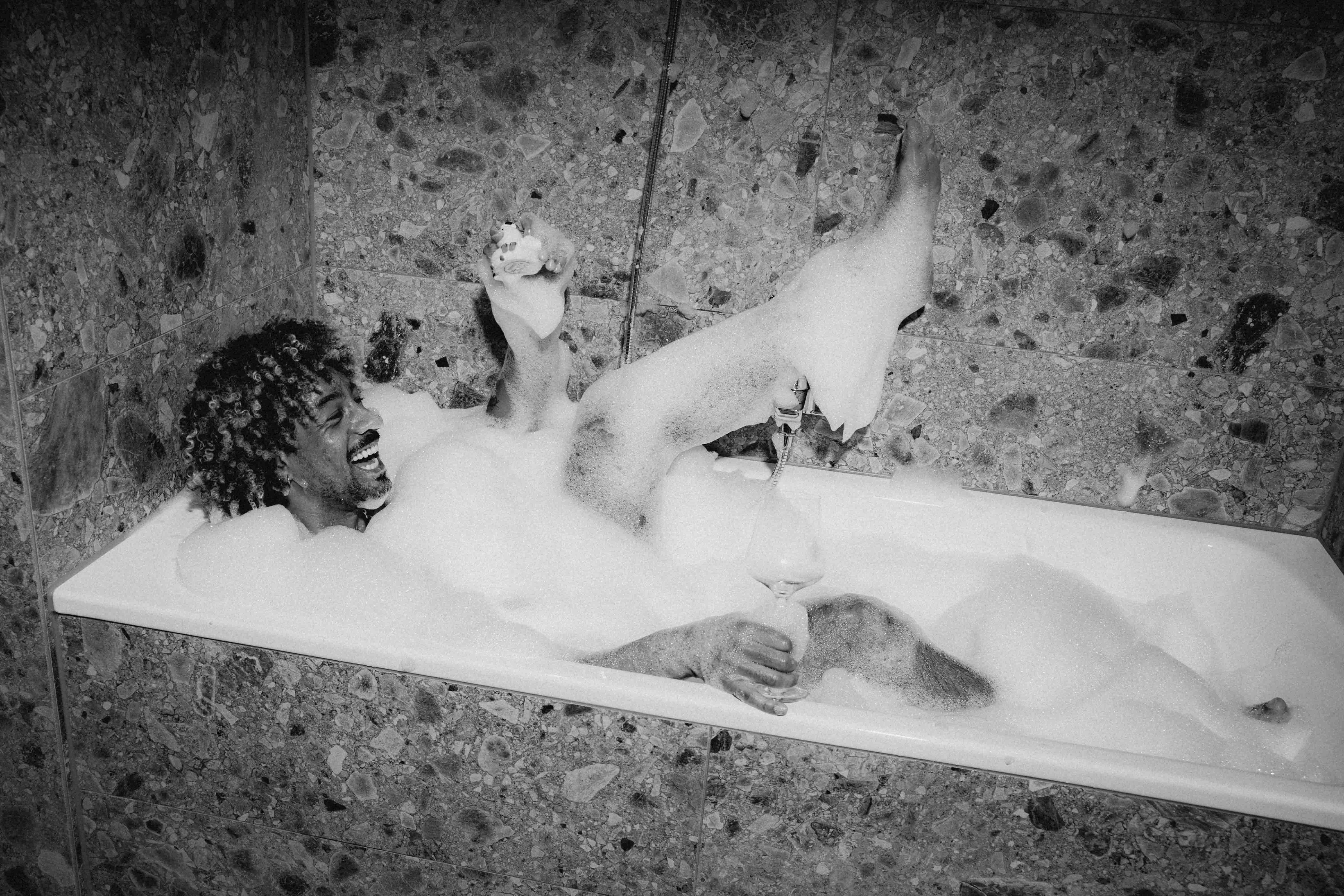 A black and white image of a neatly made bed, a bedside table, and a small trash can beside it.