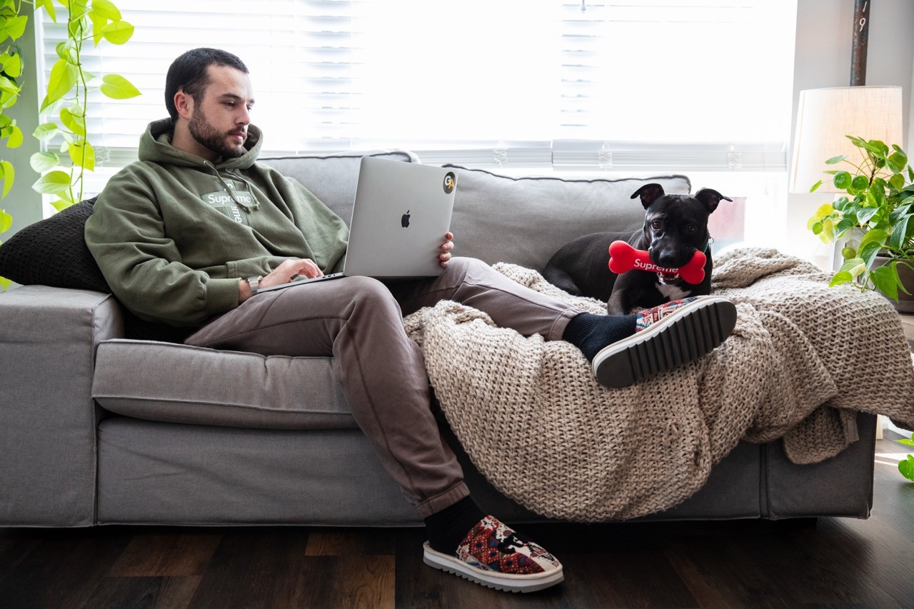 Hodinkee lifestyle feature image of a man on a couch working on a laptop next to a black dog holding a red toy.