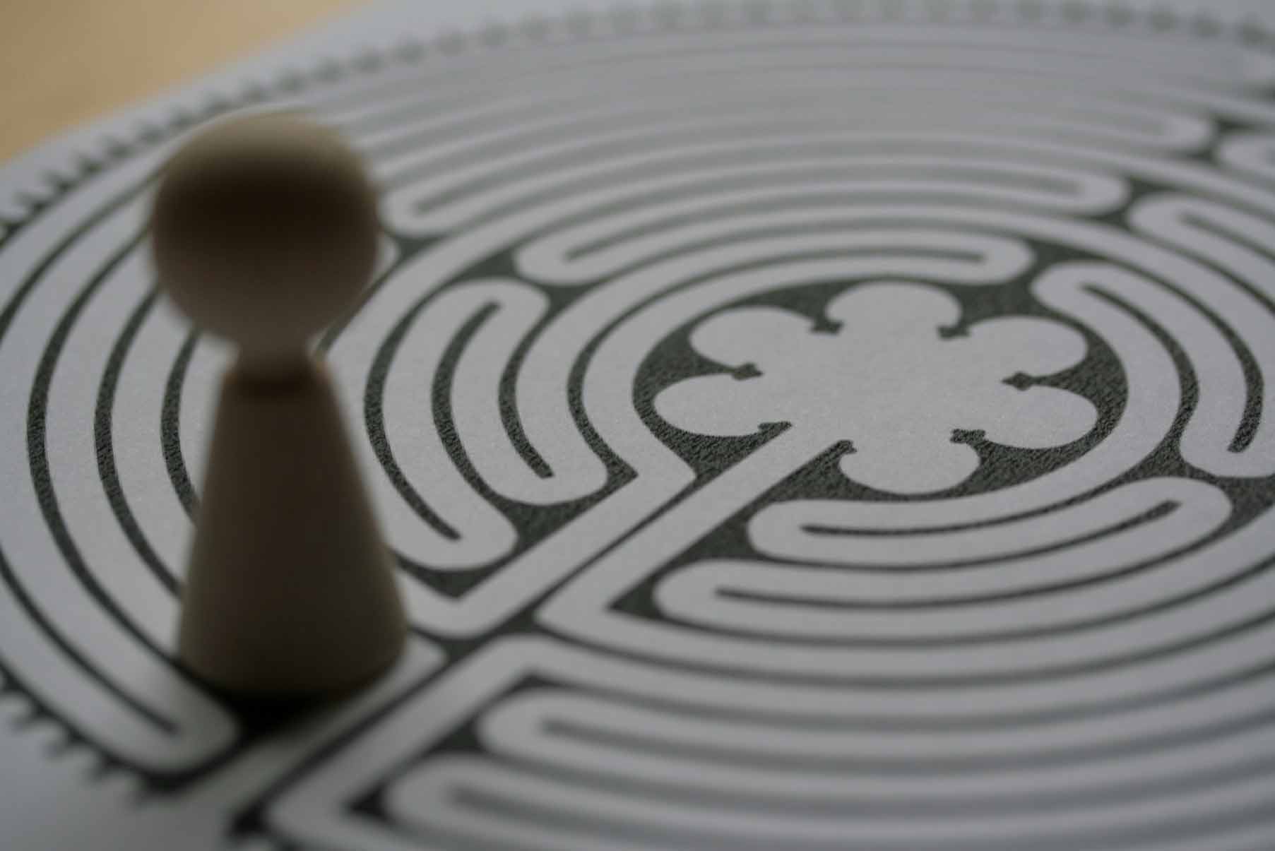 rewniany pionek stojący przed wydrukowanym labiryntem, co symbolizuje proces planowania strategii marki, rozwiązywanie problemów projektowych oraz poszukiwanie idealnego kierunku dla nowego wizerunku firmy.