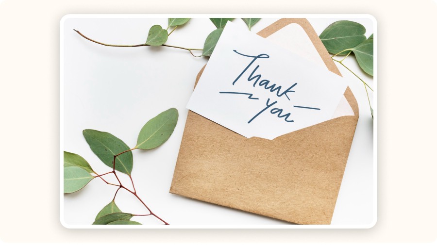 Thank-you card in kraft envelope surrounded by green leafy branches.