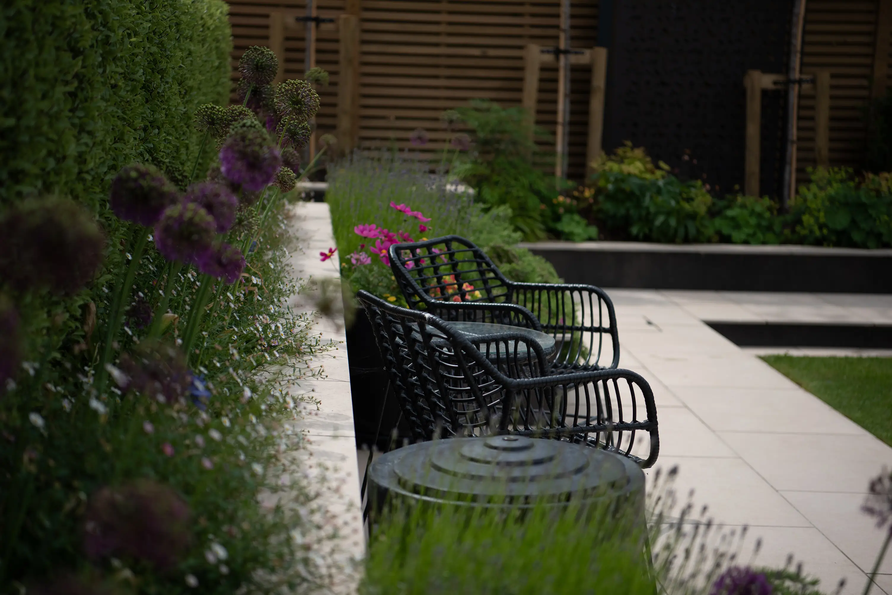 A serene garden scene featuring a pathway, greenery, and benches, surrounded by trees and flowers.