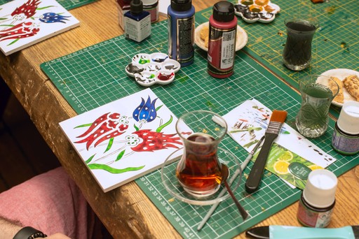 A workspace filled with painted Turkish tiles and traditional Turkish tea glasses during a tile painting workshop in Istanbul. This image captures the essence of a ceramic workshop, showcasing traditional Turkish tile art—a must-try experience in Istanbul