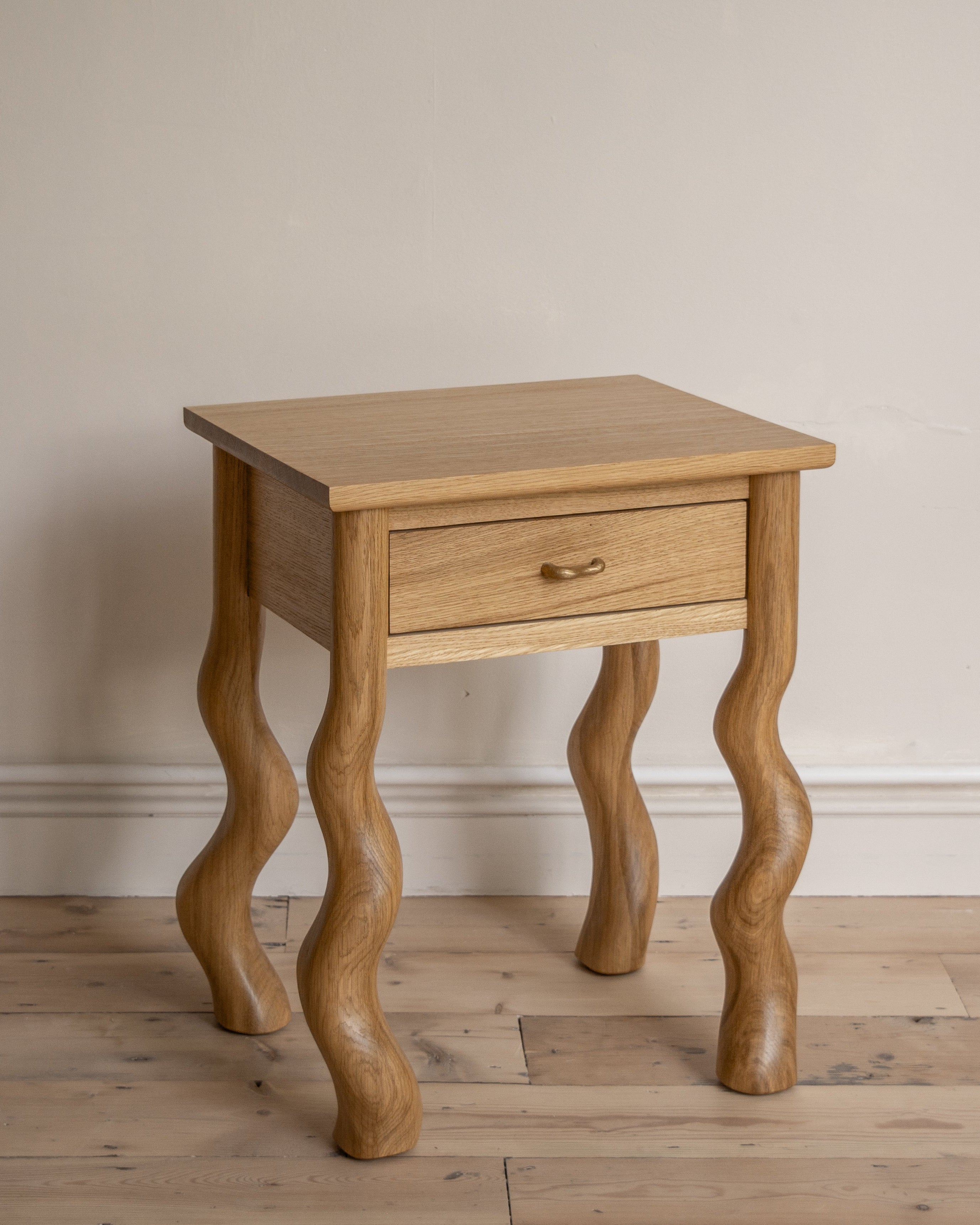 Wooden Dancing Bedside table with carved legs against a plain wall.